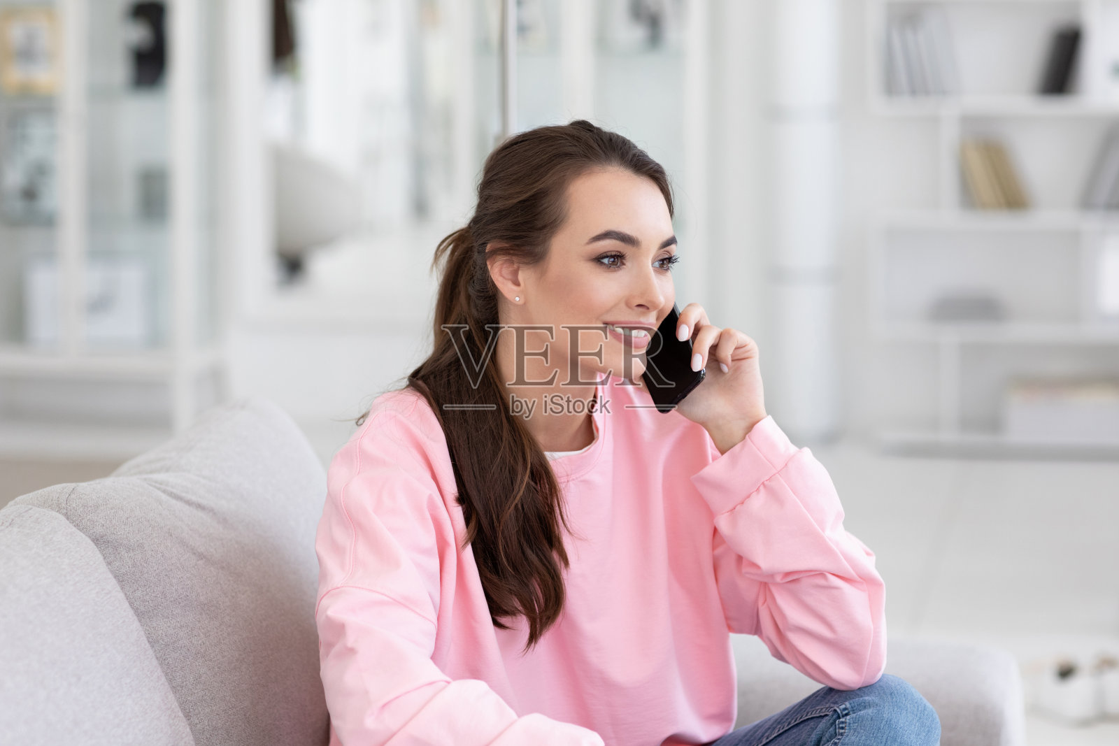 美丽冷静的女人与朋友在智能手机上交谈的特写肖像，坐在沙发上对舒适的室内。女学生在室内摆姿势照片摄影图片