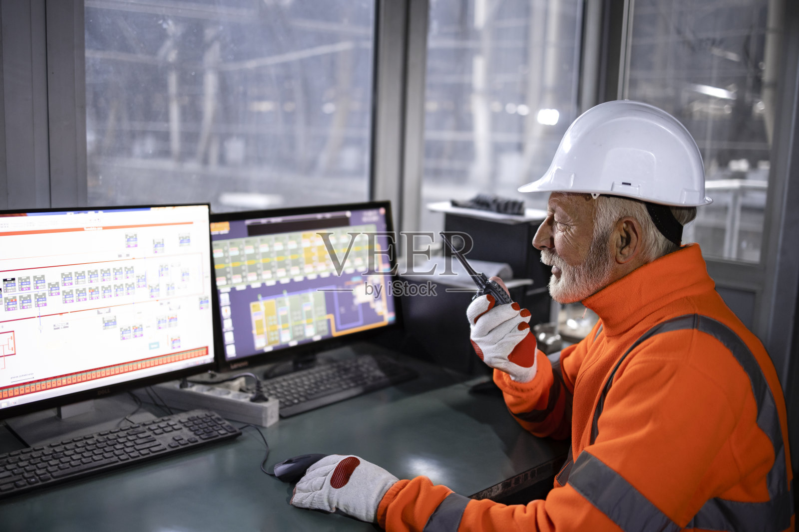 工业工人在安全设备中坐在工厂控制室里监视生产过程，用无线电通信交谈。照片摄影图片