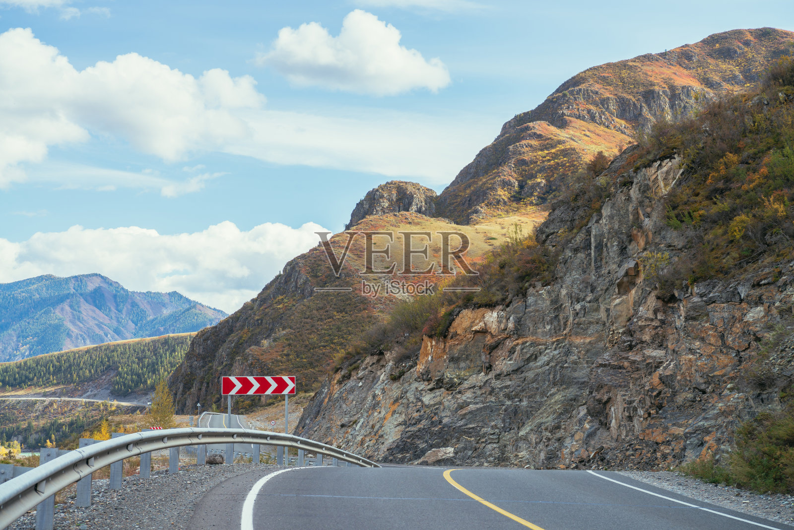 五彩缤纷的秋景，阳光下沿山路的岩石。明亮的高山风景与山路在秋天的颜色。高速公路在秋天的时候在山区。路沿着美丽的石壁。照片摄影图片