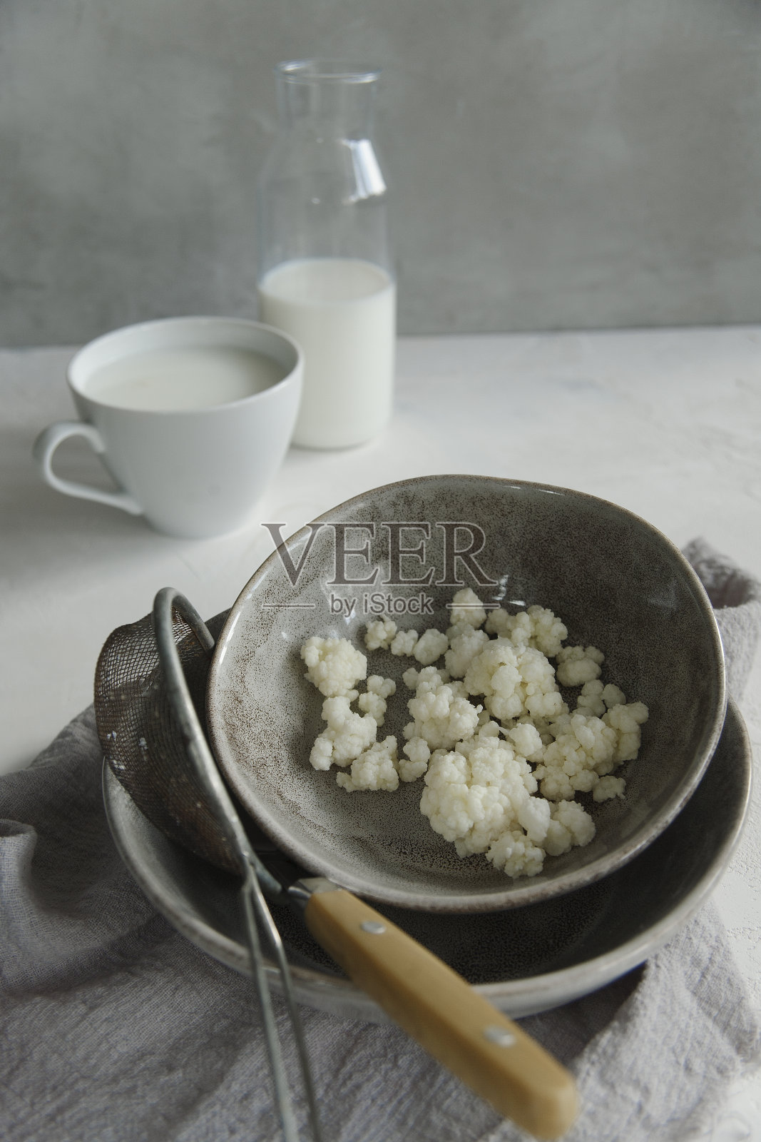 牛奶开菲尔谷物在一个灰色的盘子，一个瓶子和一杯开菲尔在白色的桌子上。照片摄影图片