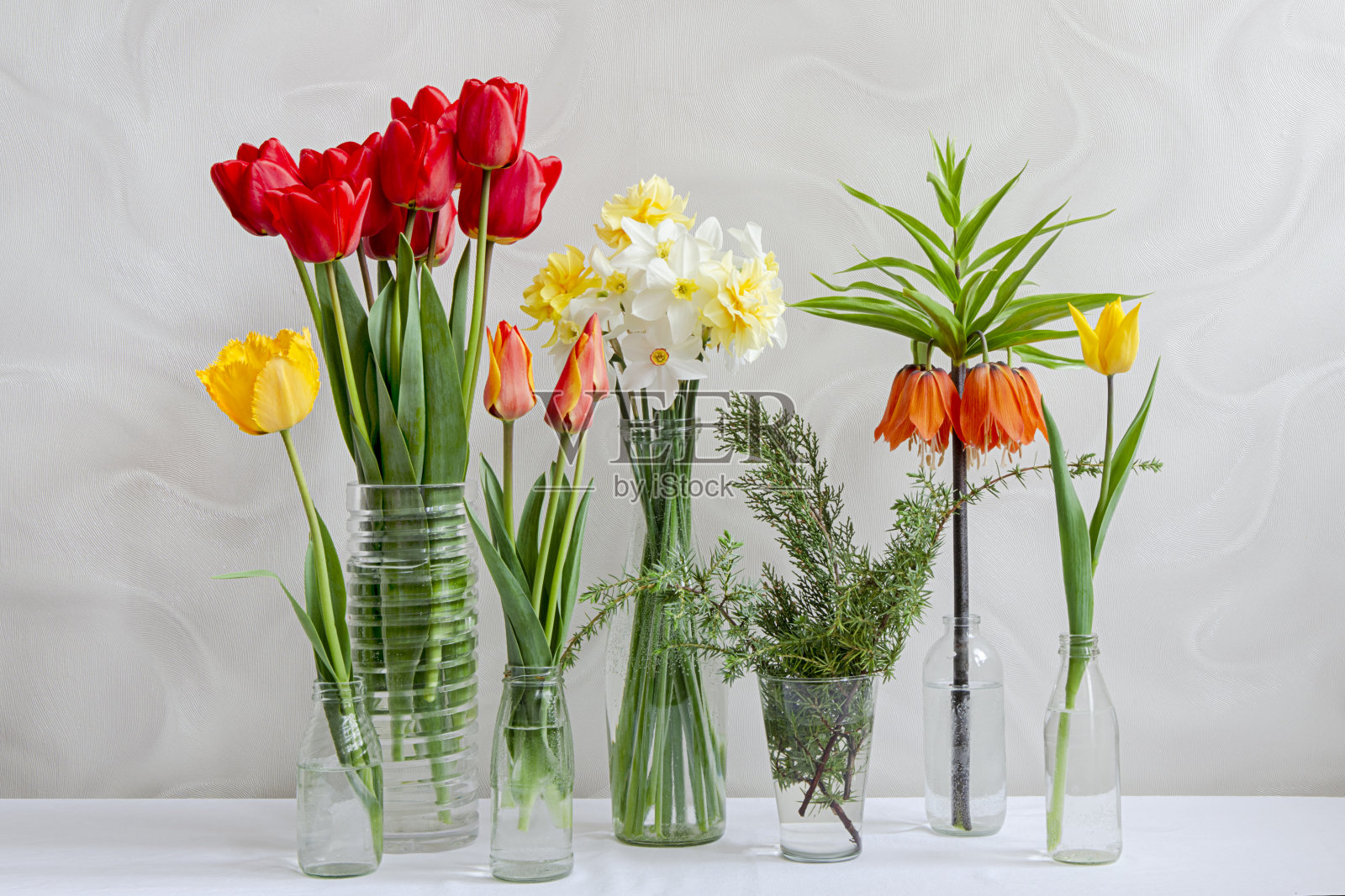 桌上透明的花瓶里放着不同的春花。照片摄影图片