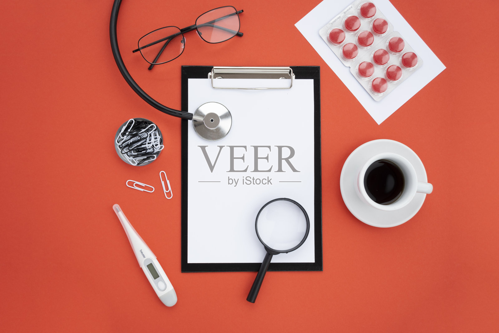 俯视图，红色背景上的医疗配件。药片，听诊器，眼镜，药丸，药品，咖啡杯，放大镜。平坦的躺,模型照片摄影图片