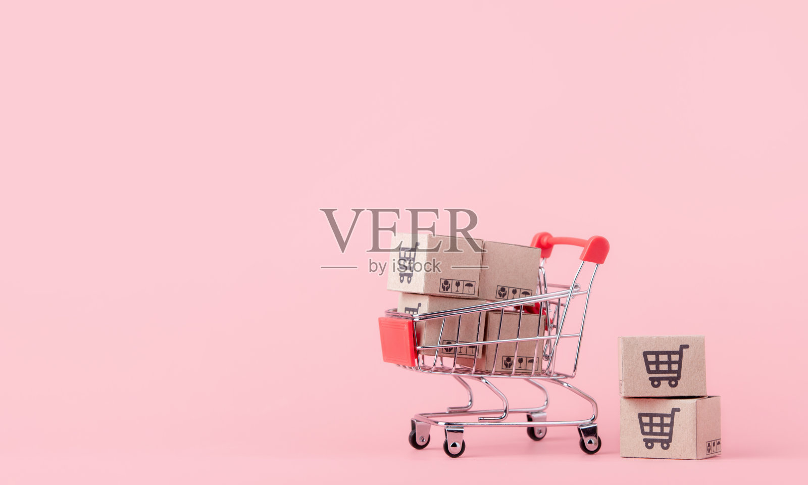 购物概念:红色购物车中的纸箱或纸盒，粉色背景。网上购物的消费者可以在家购物和送货上门。与复制空间照片摄影图片