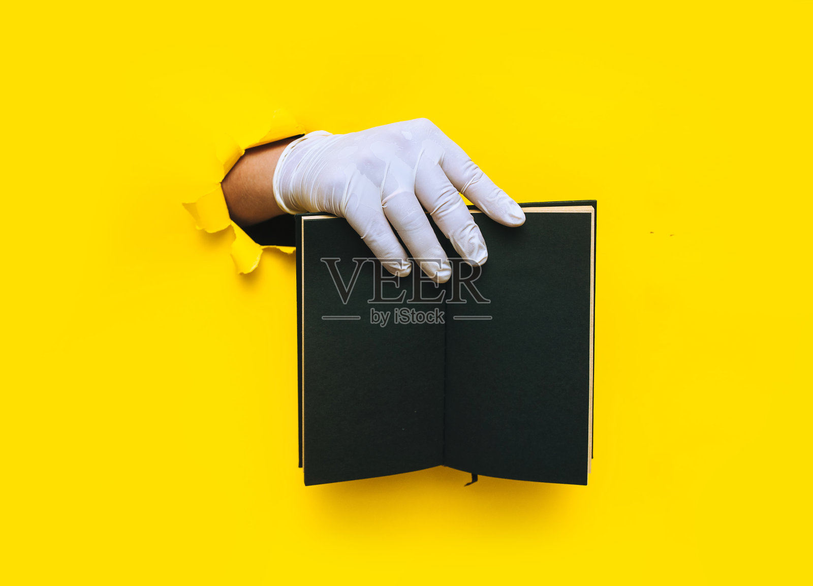 一位医生戴着白色乳胶医用手套，右手拿着黄色背景的黑色手工笔记本。撕纸与复印空间，模拟。概念文本放置，黑名单。照片摄影图片
