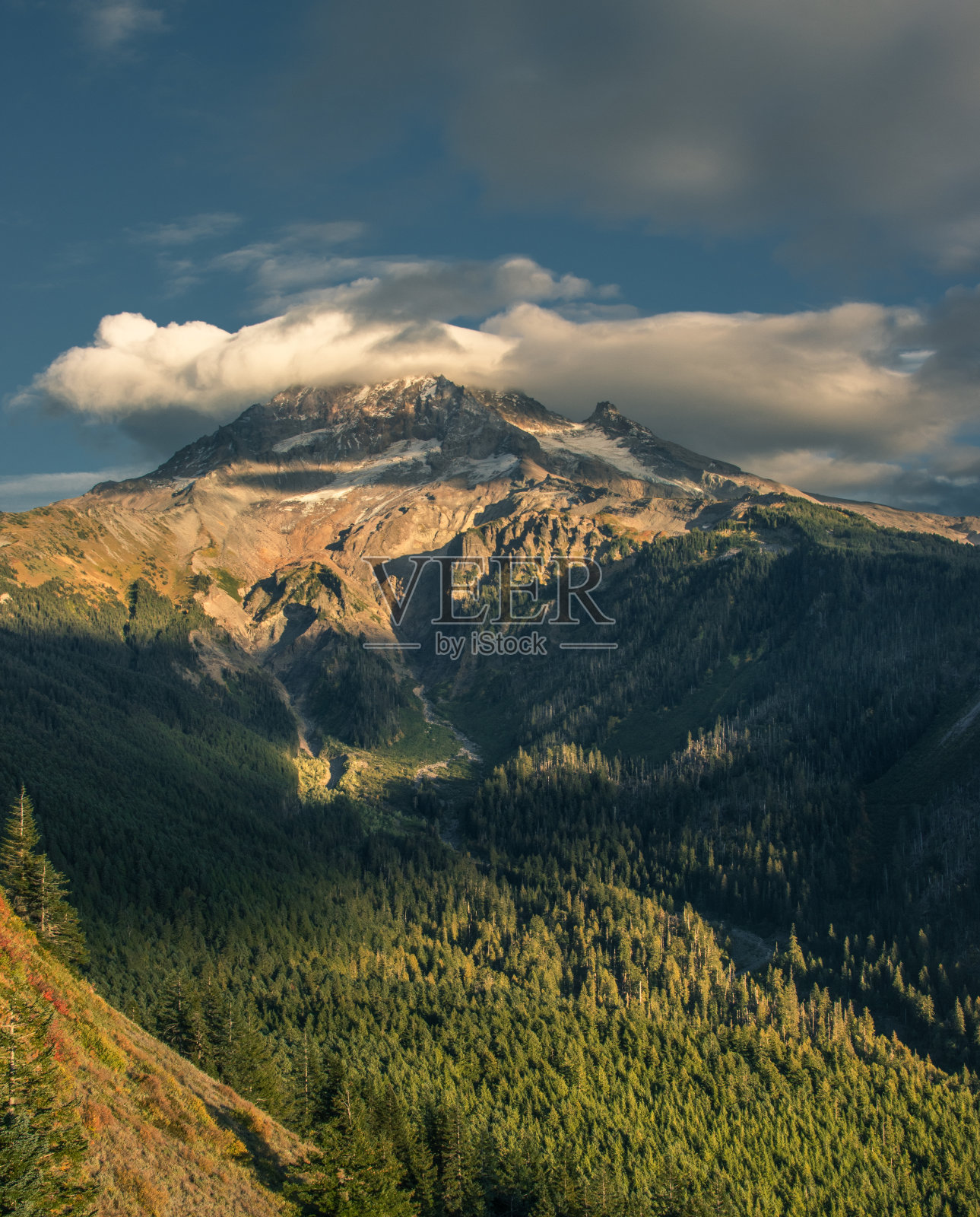 在秋天美丽的日落时分，一片透镜状的云拥抱着被白雪覆盖的胡特山。照片摄影图片