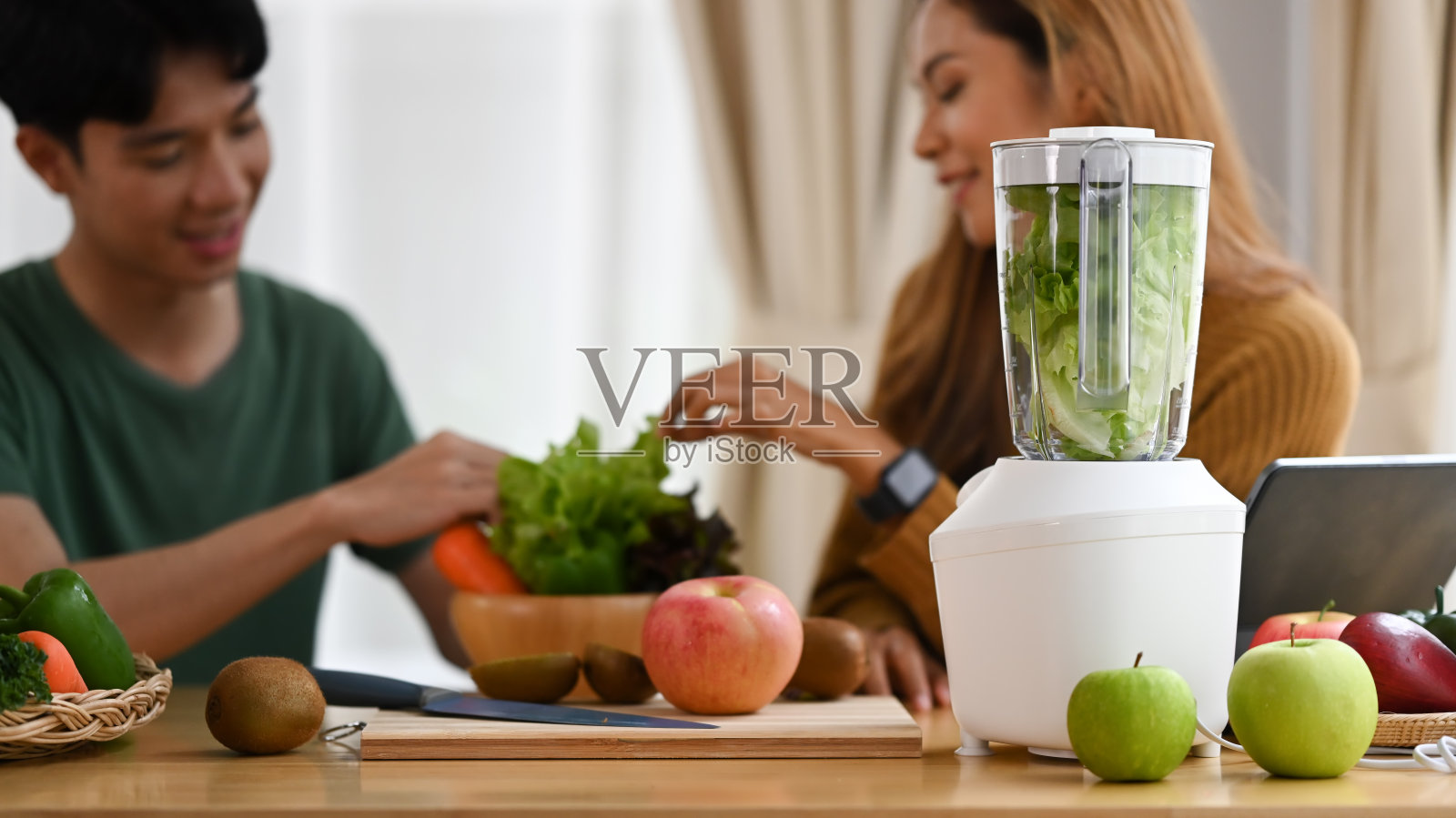 快乐的年轻夫妇用新鲜的蔬菜和水果在厨房做绿色排毒奶昔。照片摄影图片
