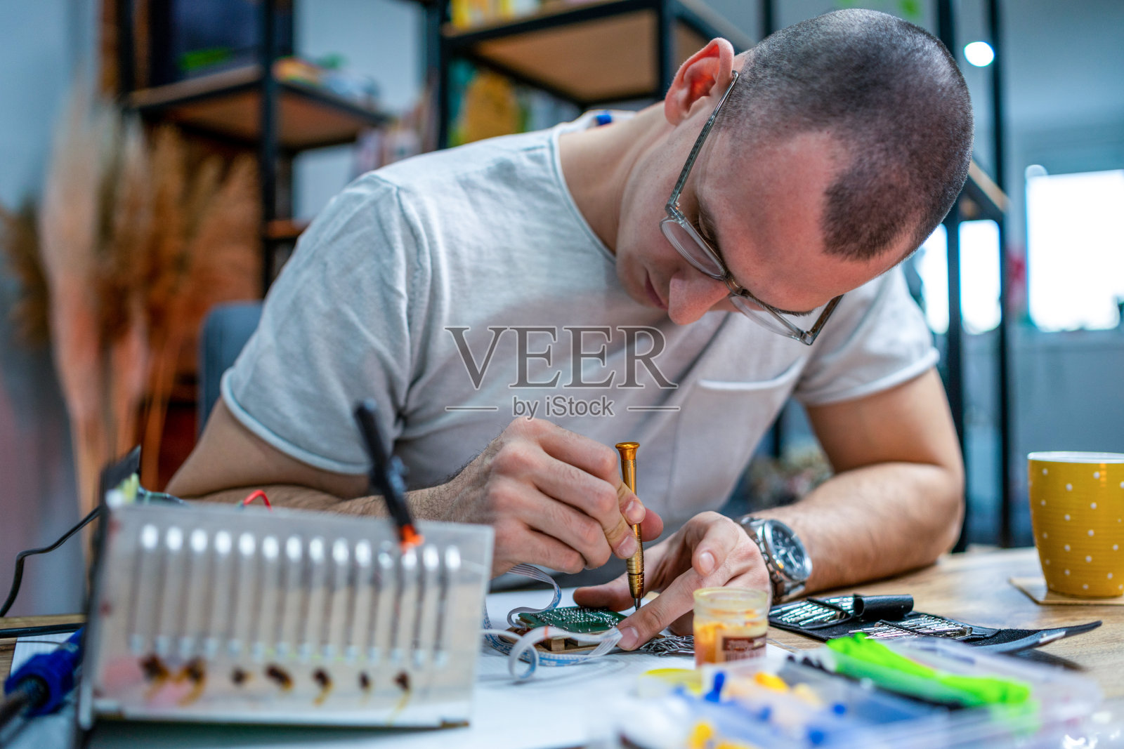 这位年轻的电子工程师检查、修理并完成了交给他修理的主板。他使用工具，在家庭环境中工作。照片摄影图片