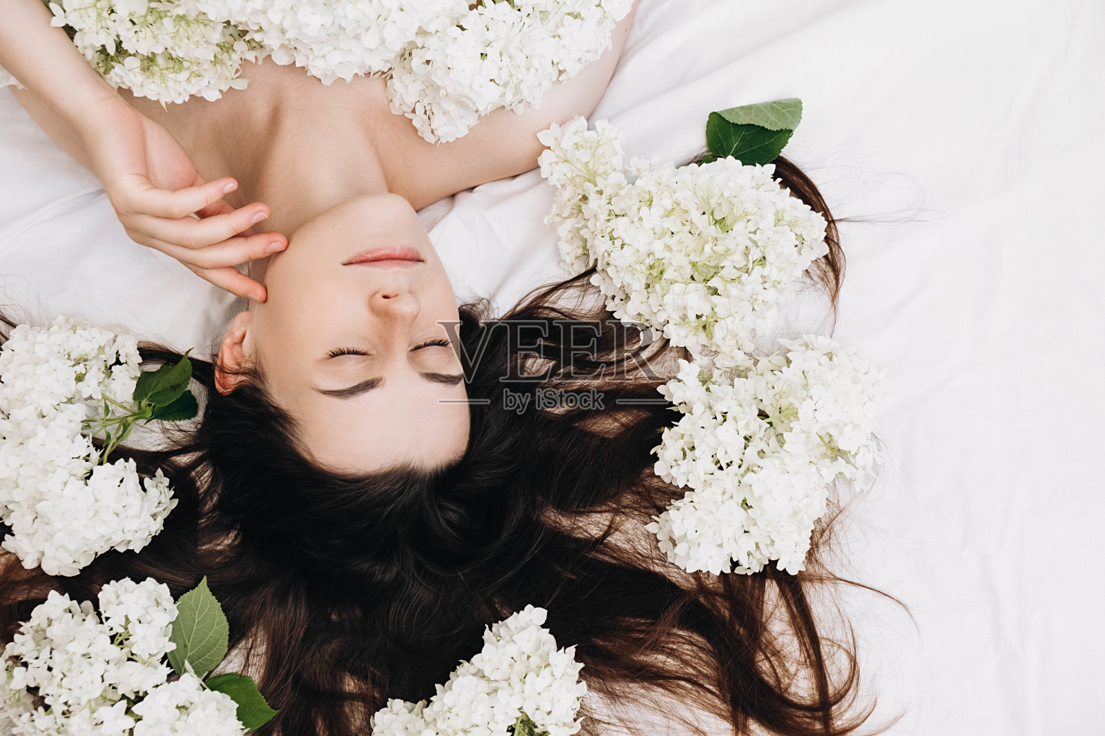 俯视图浪漫微笑美丽的千禧女士与清洁纯净的皮肤美容后，躺在床上春天新鲜的白花。皮肤美容保健理念。身体部位及性质照片摄影图片