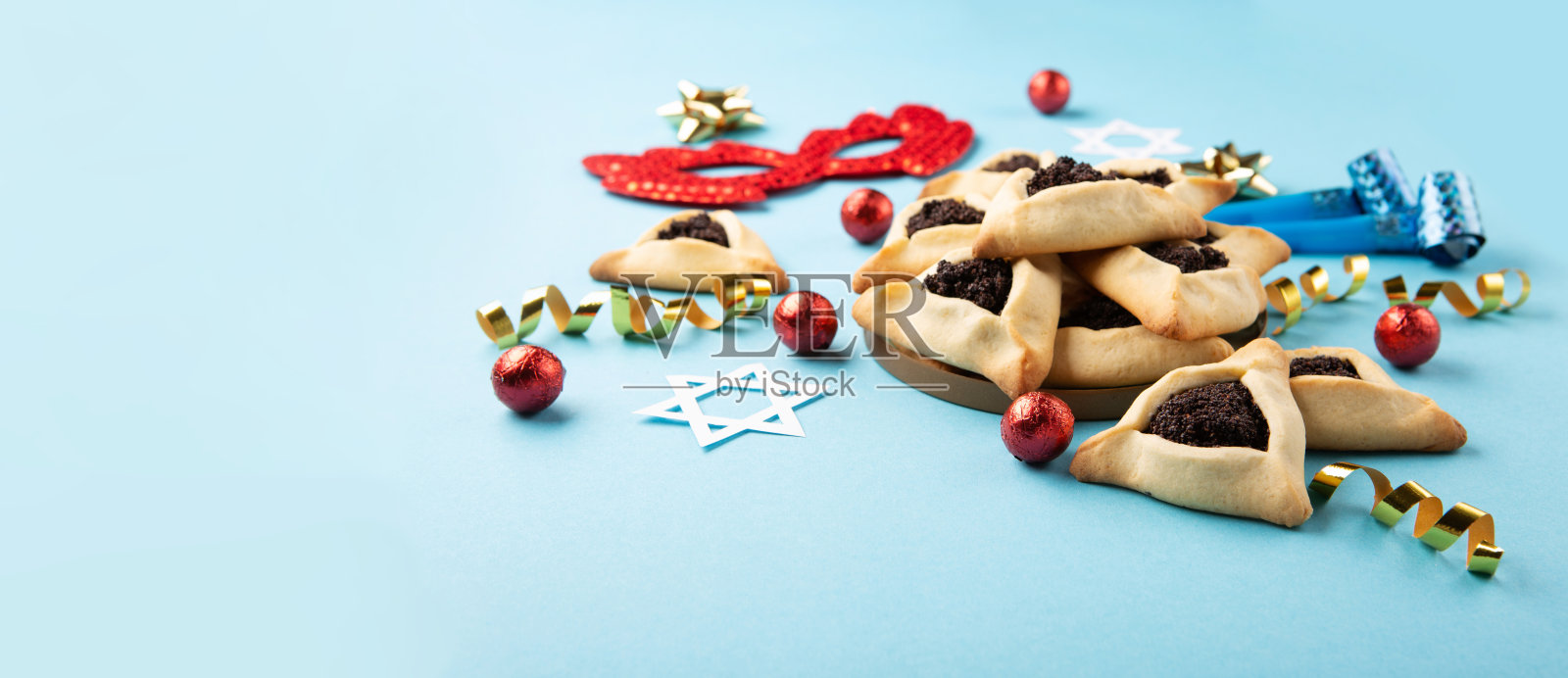 普里姆自制的哈曼塔什饼干，红色的狂欢节面具，噪音制造者，糖果和派对装饰在蓝色的背景。照片摄影图片