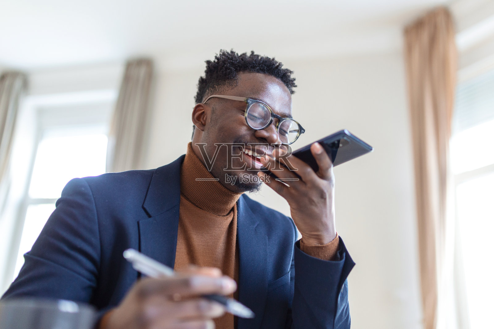 Arfican商人写笔记在记事本上，而谈话通过免提电话从工作空间。语音识别的概念。免提通信。照片摄影图片