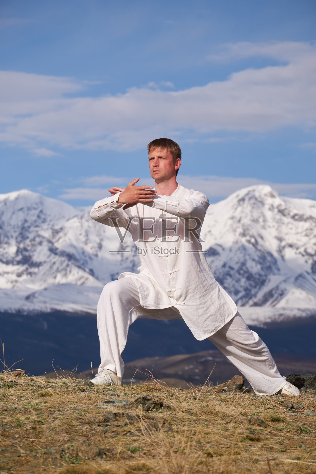 身着白色运动服的武术大师在雪山背景下训练功夫。照片摄影图片