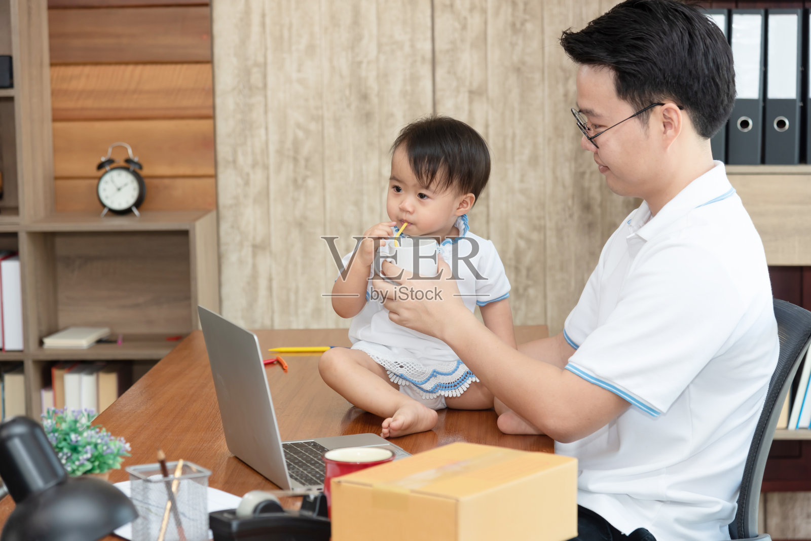 工作繁忙的商人，还要照顾自己的孩子。多任务的亚洲父亲，在家工作的概念。照片摄影图片