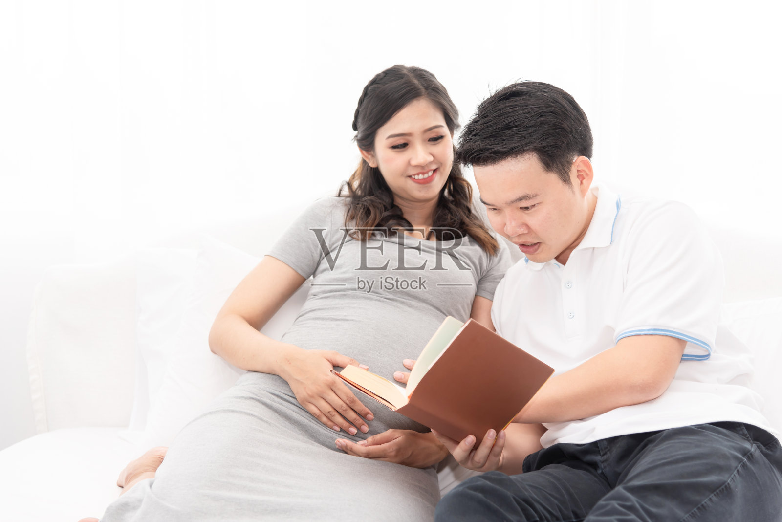 亚洲新爸爸和妻子在一起，兴奋的爸爸期待着新生儿的到来。丈夫读着书给妻子听，为新生儿做准备。照片摄影图片