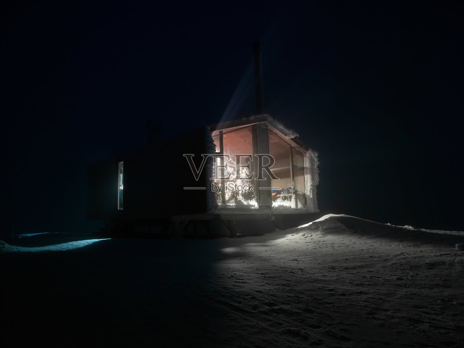 冬夜的小屋。冬日的草地上，雪堆成山，小屋的夜窗透出侧光。照片摄影图片