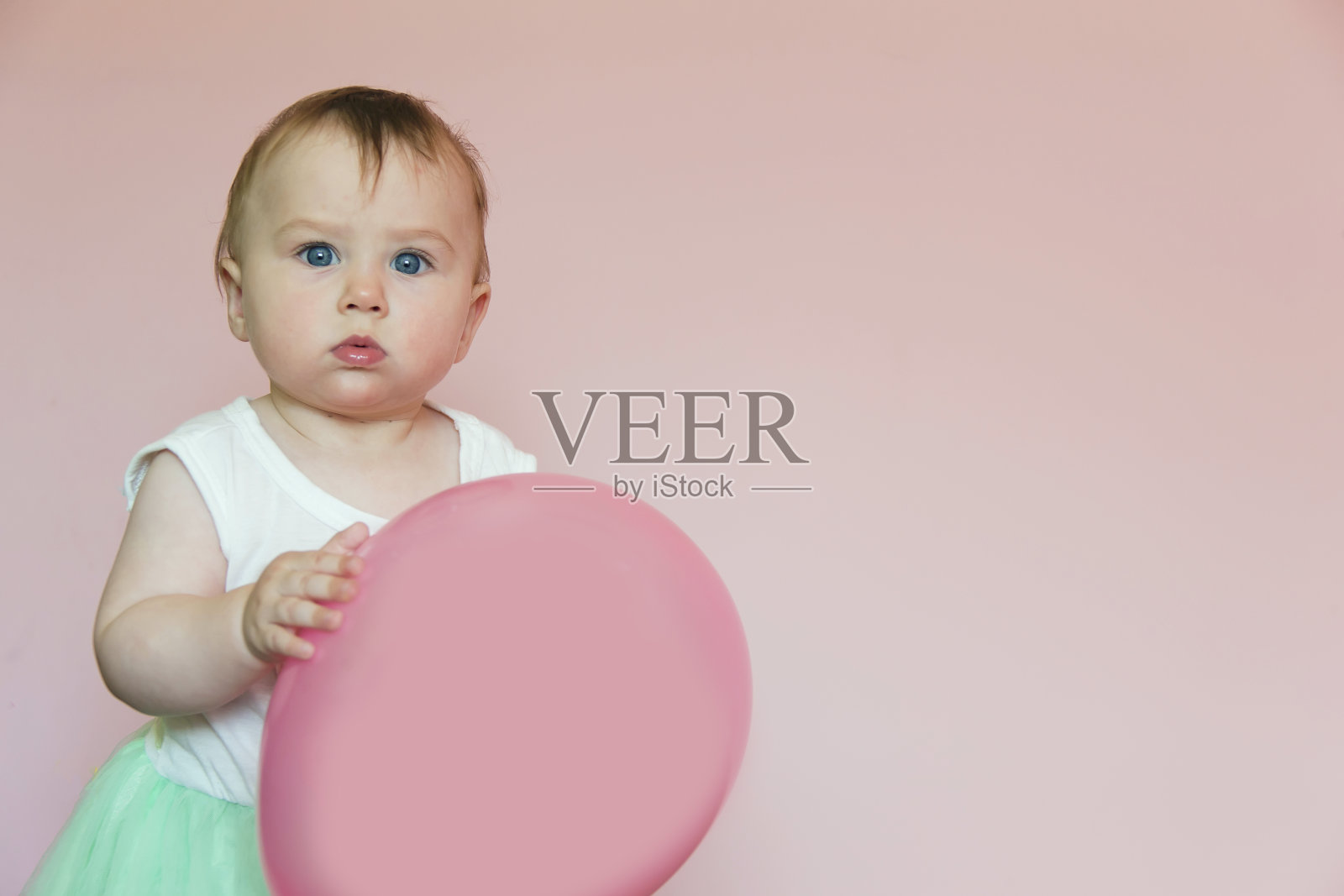 一个一岁的小女孩手里拿着一个粉红色的充气球。照片摄影图片