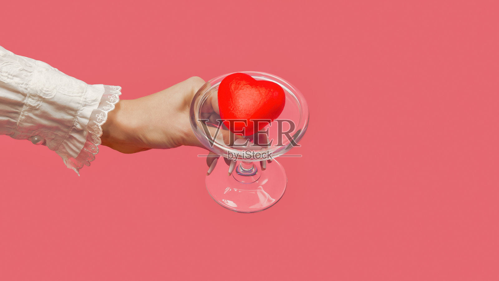 一个女人的手在玻璃盘子上盛着一颗红心。珊瑚背景上的美丽礼物。最小的情人节或周年纪念概念。创意爱情或情人节的概念。喜欢甜点。照片摄影图片