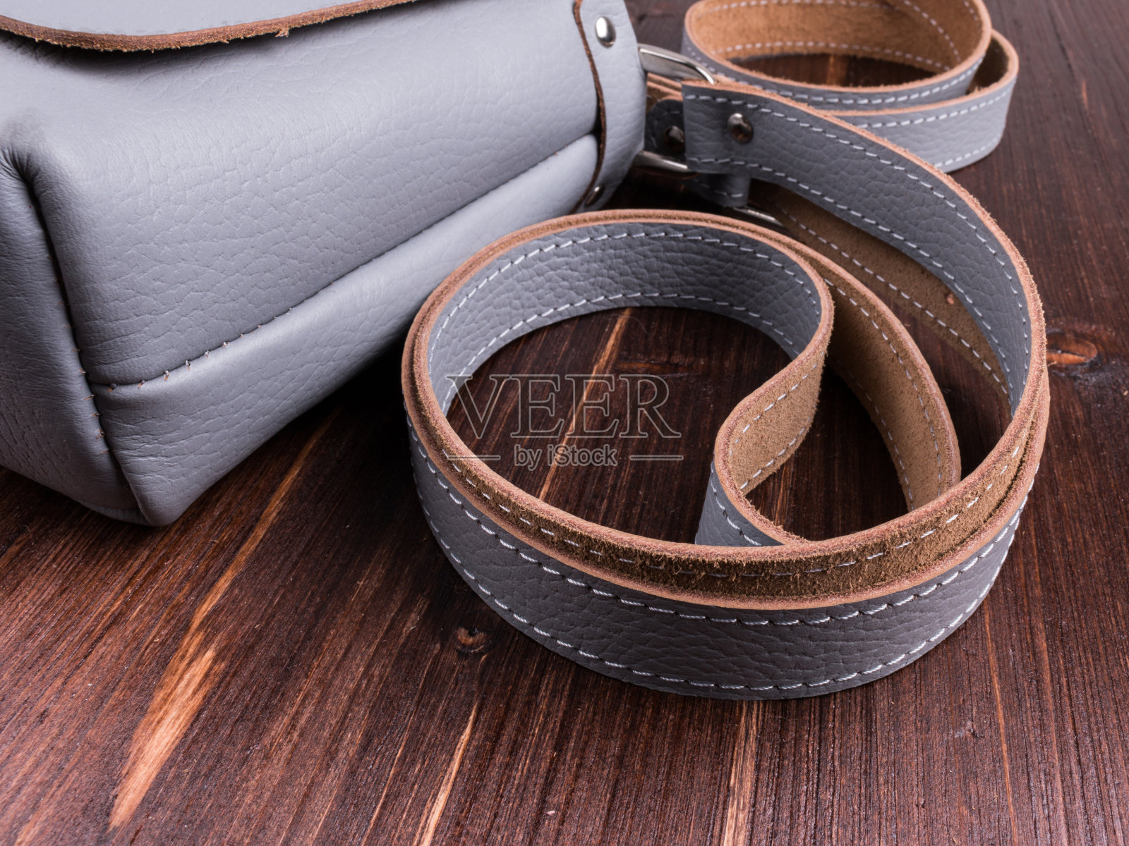 棕色木桌上灰色皮革斜挎包的特写镜头。包由真正的纹理皮革与肩带照片摄影图片