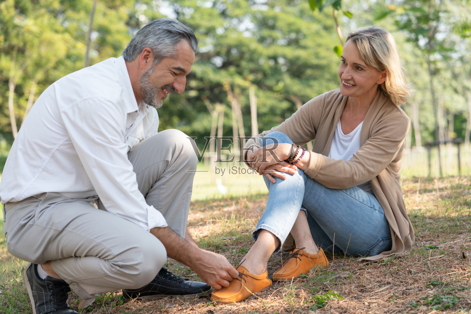 可爱的夫妇，资深丈夫帮助他的妻子系鞋带，一起坐在公园里。老年人养老放松理念照片摄影图片