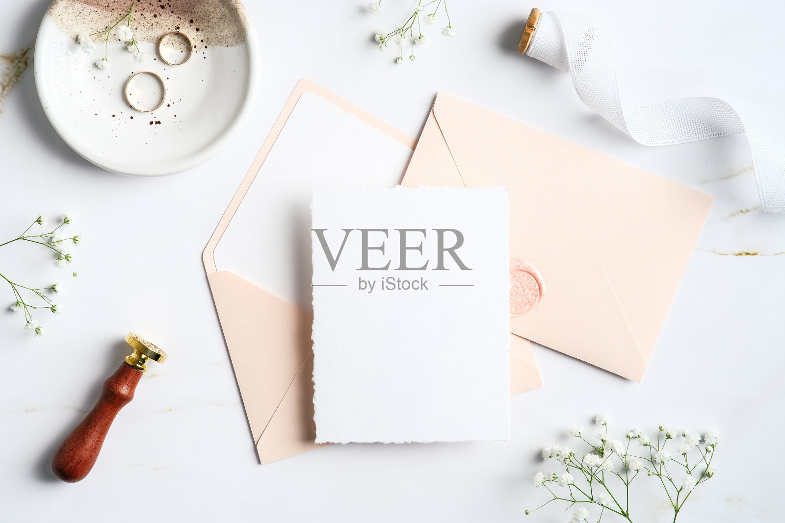 婚礼文具放在大理石桌子上。空白的婚礼请柬模型，粉彩信封，戒指，蜡封邮票，丝带，花。平躺，顶视图，复制空间。照片摄影图片