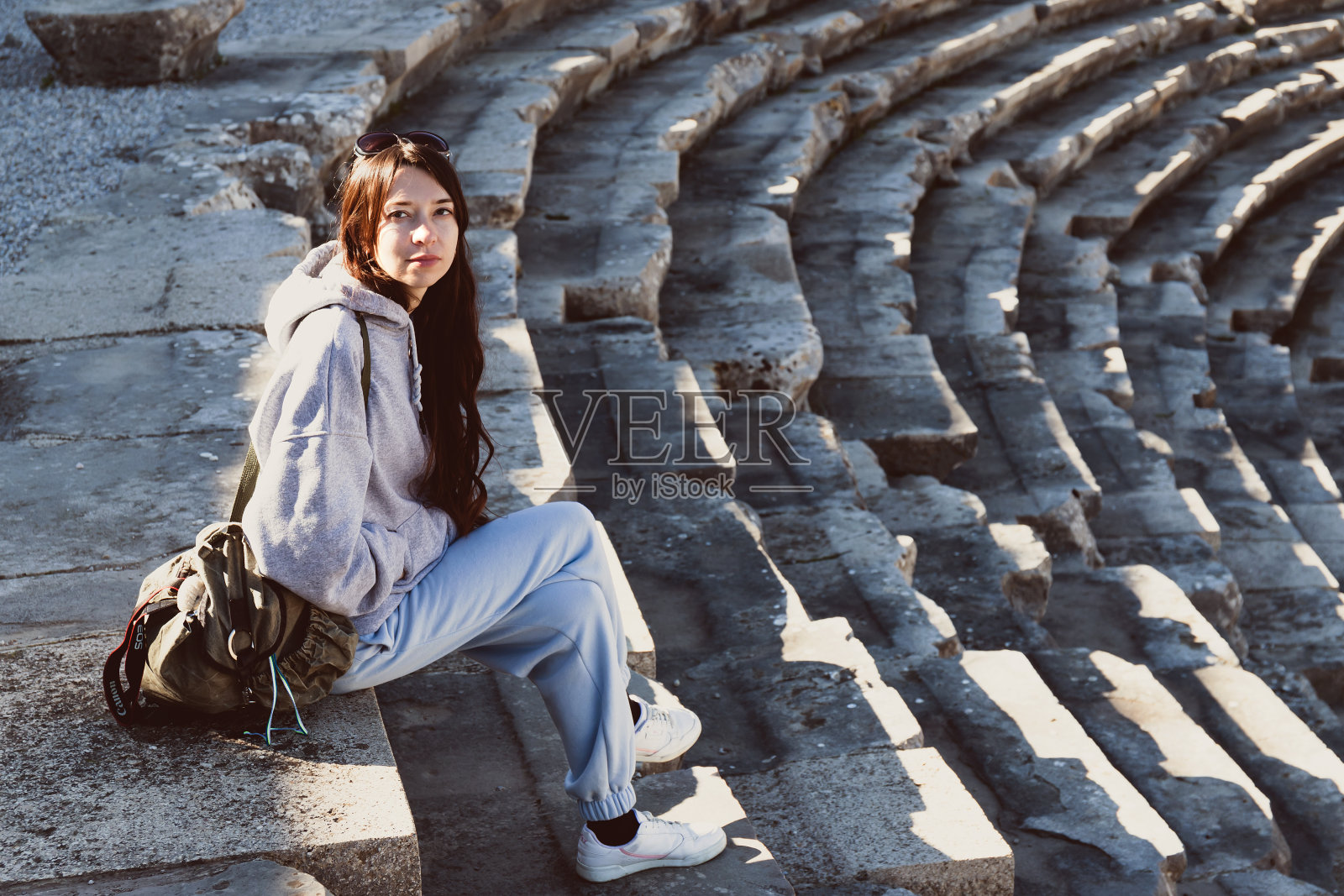 深思熟虑的孤独漂亮的年轻女子坐在古老的圆形剧场的台阶上。照片摄影图片