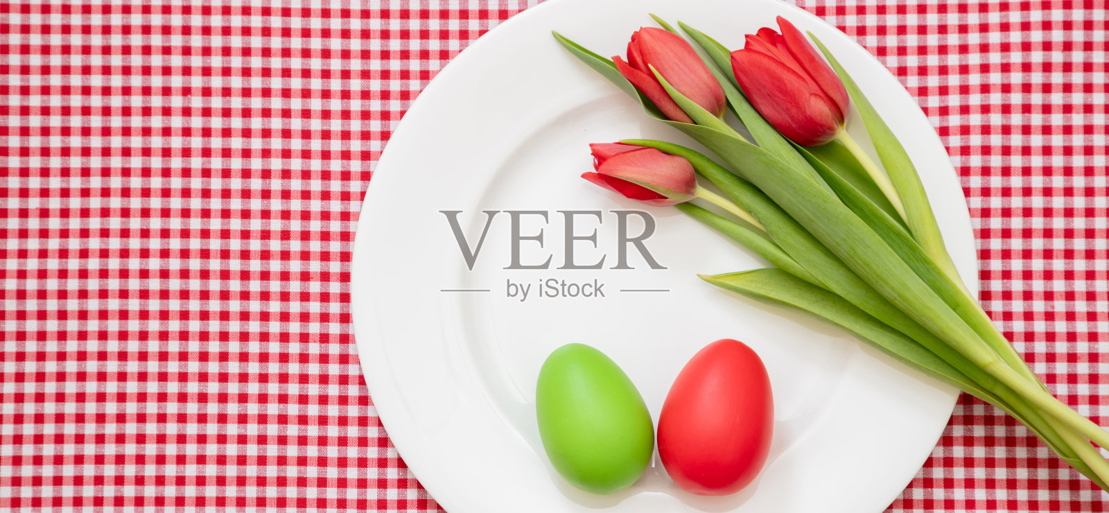 复活节表。鸡蛋红，绿色和郁金香装饰白色盘子，格子桌布，头顶照片摄影图片