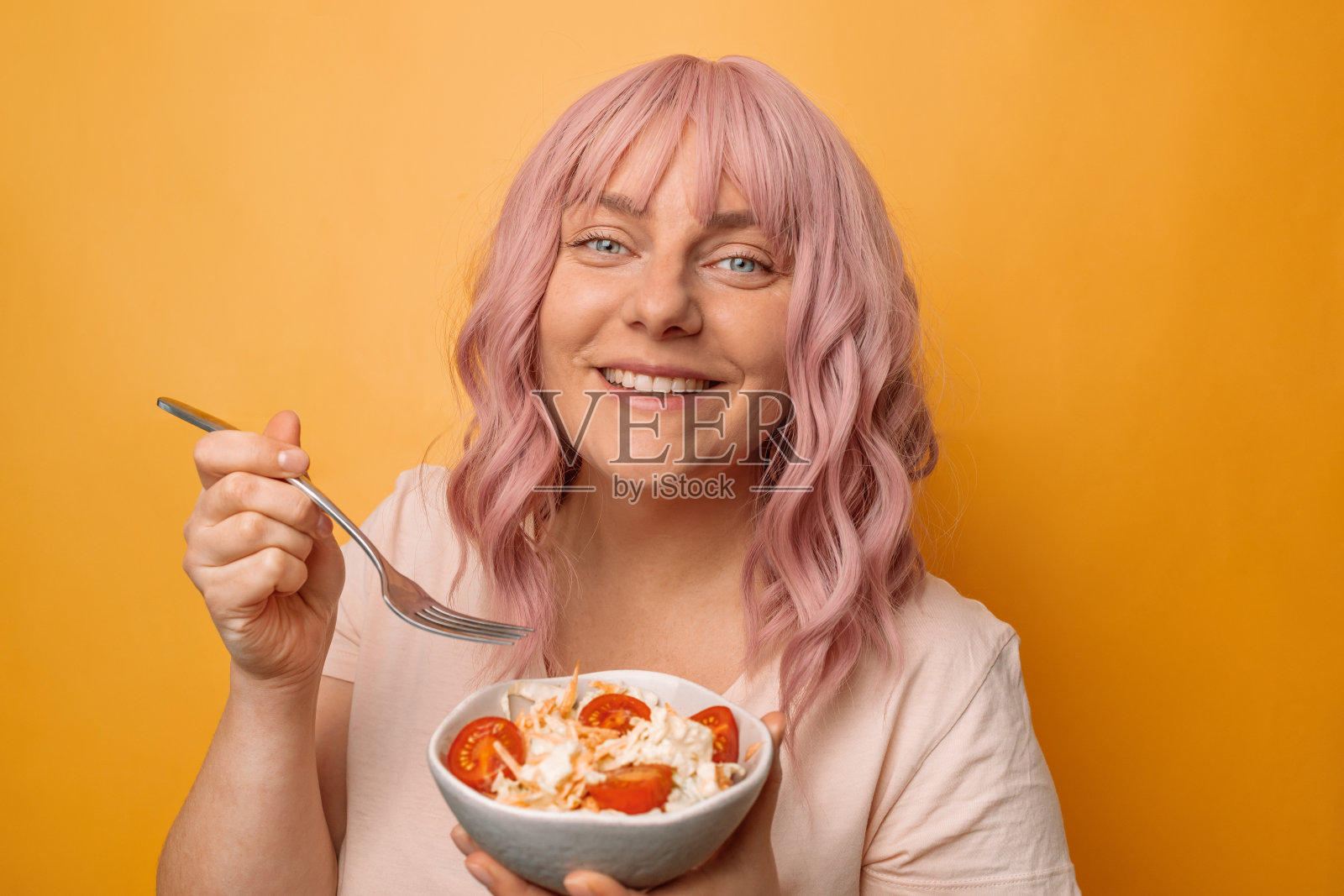 快乐的年轻女子吃新鲜健康的素食沙拉与许多蔬菜黄色背景。健身和健康的生活方式理念。照片摄影图片