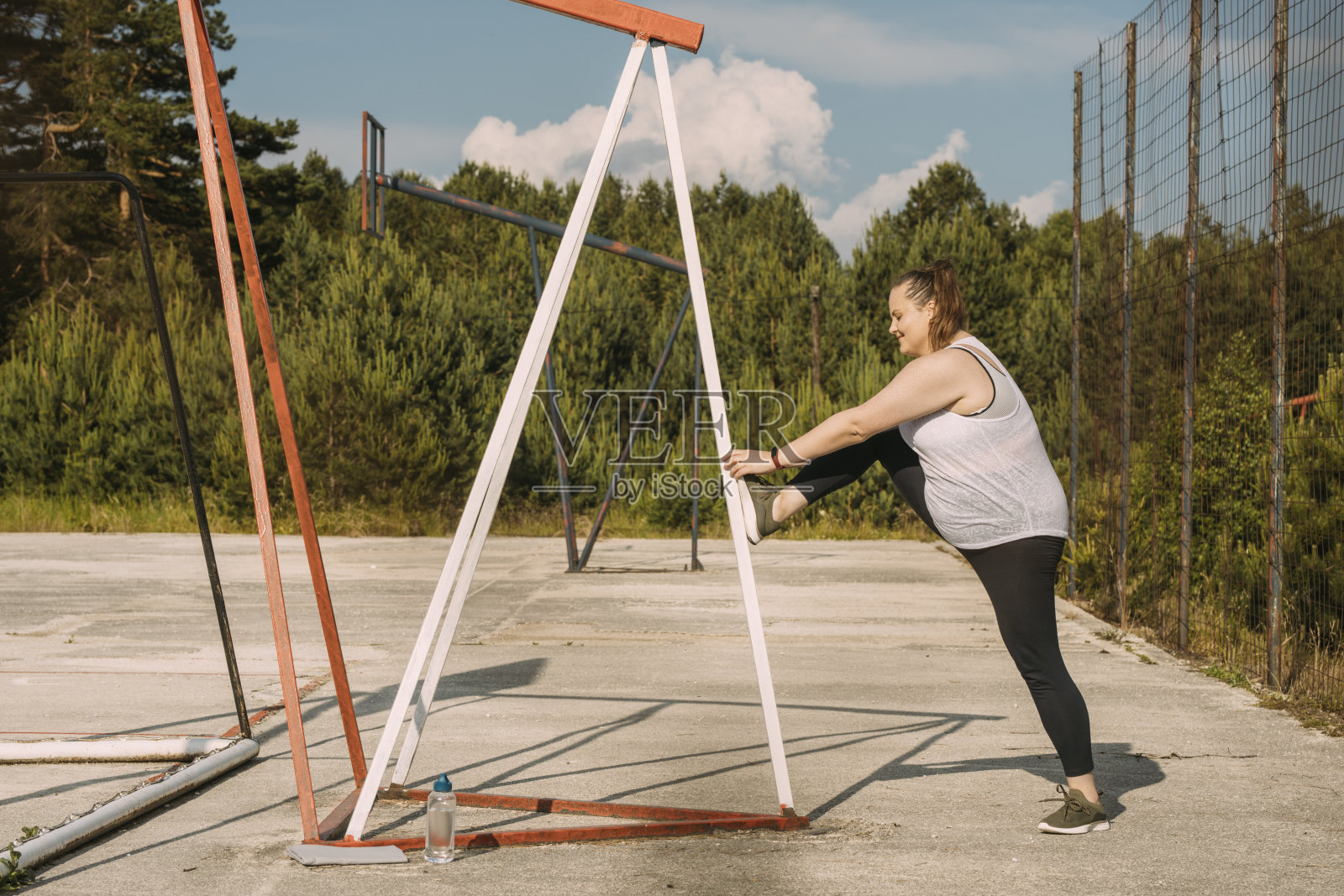 一个超重的女人微笑着在户外篮球场上伸展身体照片摄影图片