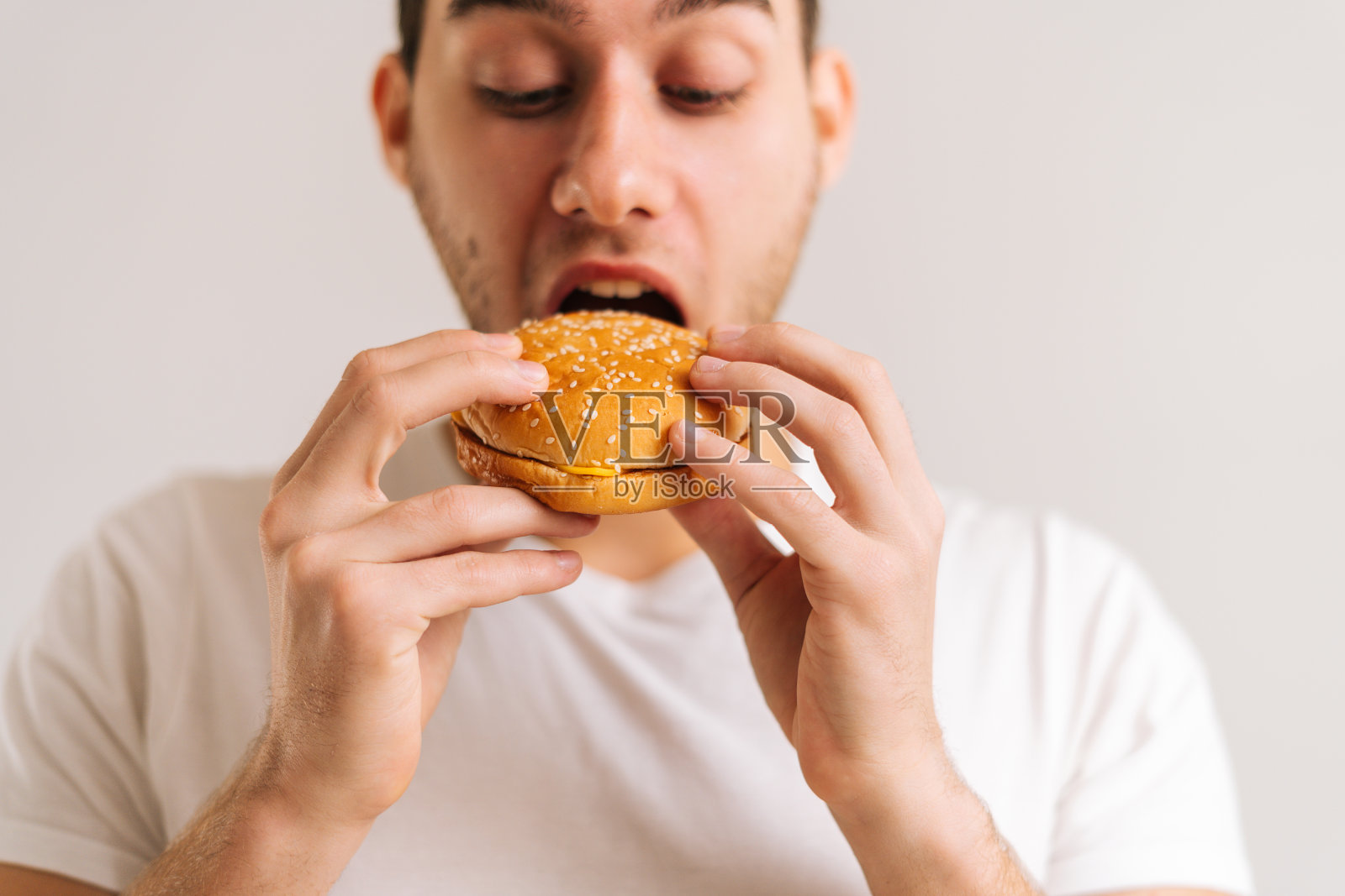 近距离的英俊的年轻男子咬吃美味的汉堡在白色孤立的背景。照片摄影图片