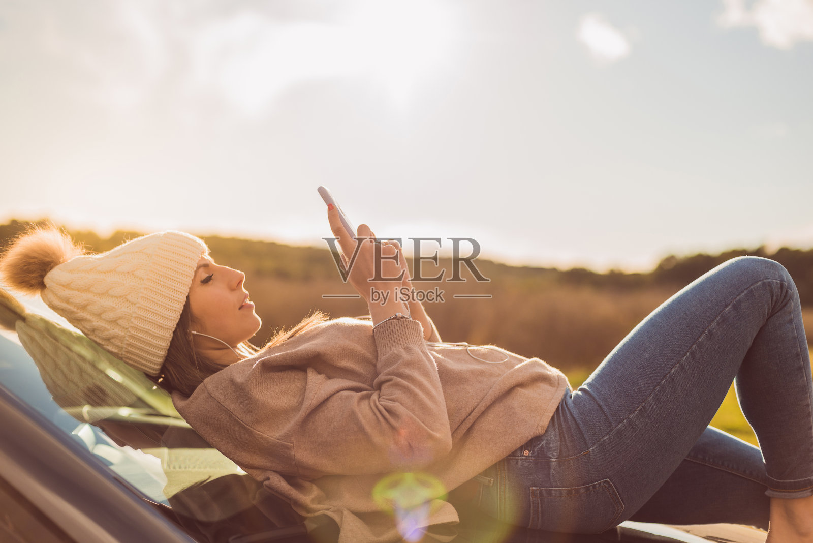 日落时分，一个女孩躺在汽车引擎盖上听音乐。她很幸福，在恋爱中。情人节。爱情,幸福。照片摄影图片