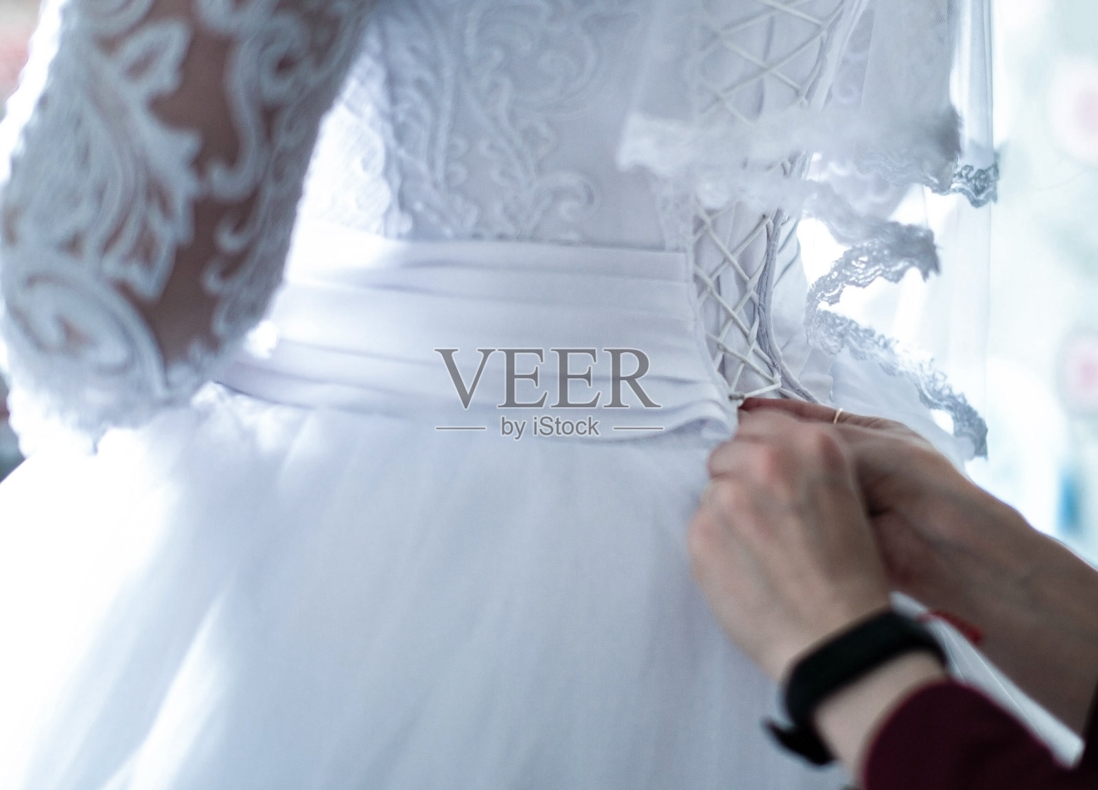 伴娘为新娘系上紧身衣。蕾丝面纱。新娘白色礼服。未来妻子的束身衣上的鞋带。一件华丽优雅的连衣裙。照片摄影图片