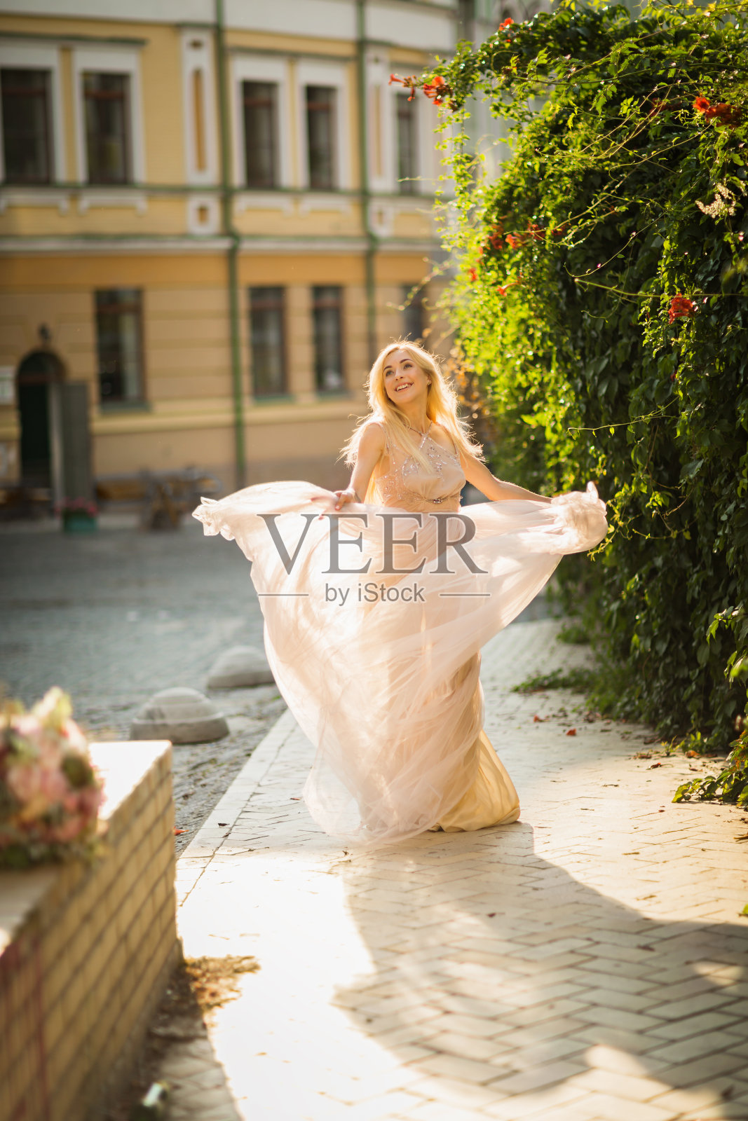 美丽微笑的年轻女子，长长的金发，穿着飘逸轻盈的衣服在街上奔跑照片摄影图片