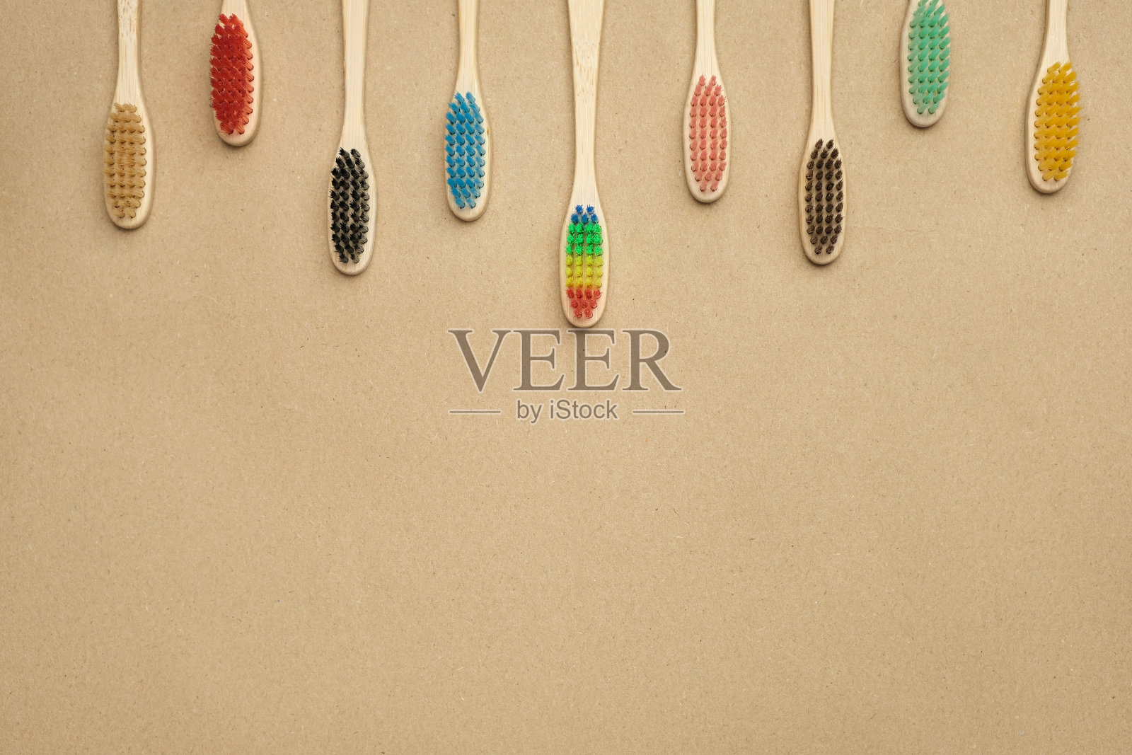 一串五颜六色的竹制牙刷挂在画框的顶部。在牛皮纸上，俯视图，拷贝空间照片摄影图片