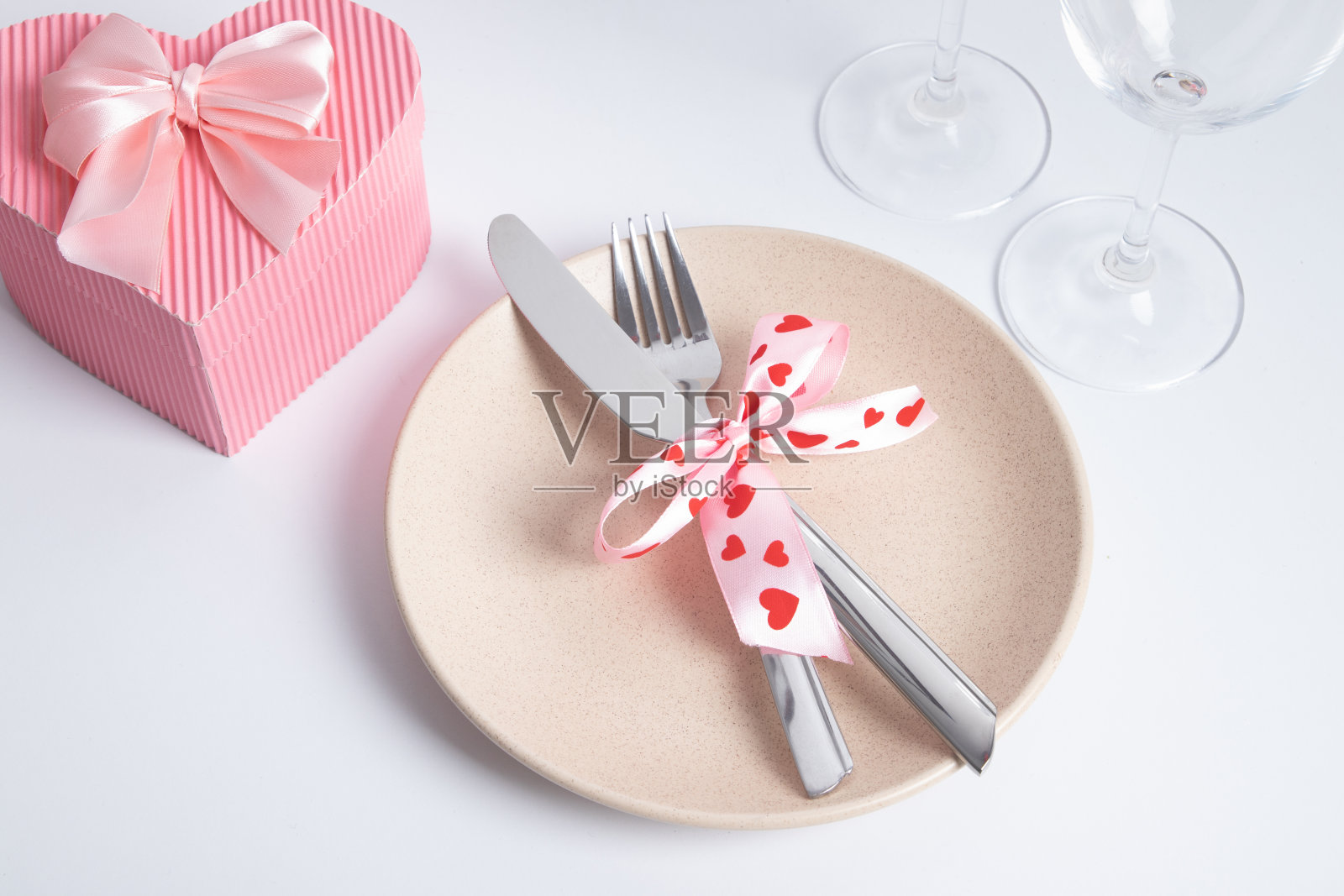 白色的桌子上摆放着粉红色心形礼盒的餐具和盘子。情人节的浪漫晚餐照片摄影图片