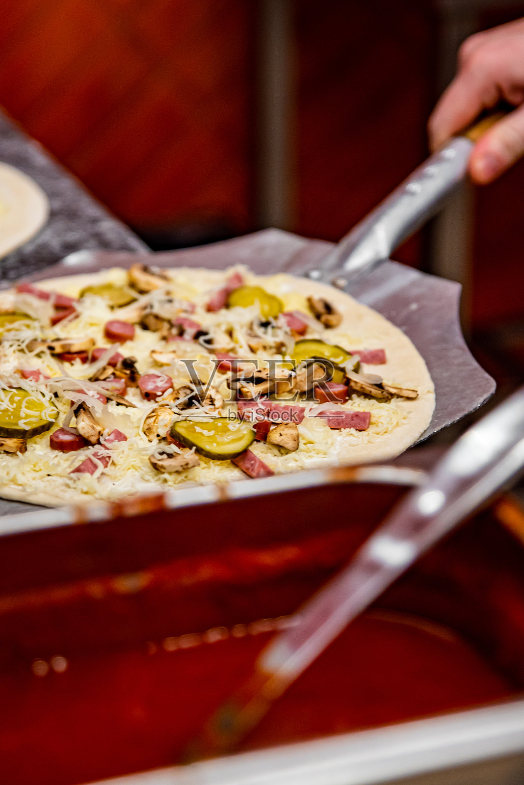 面包师在厨房做披萨的手。用铲子把它放到烤箱里烤。照片摄影图片