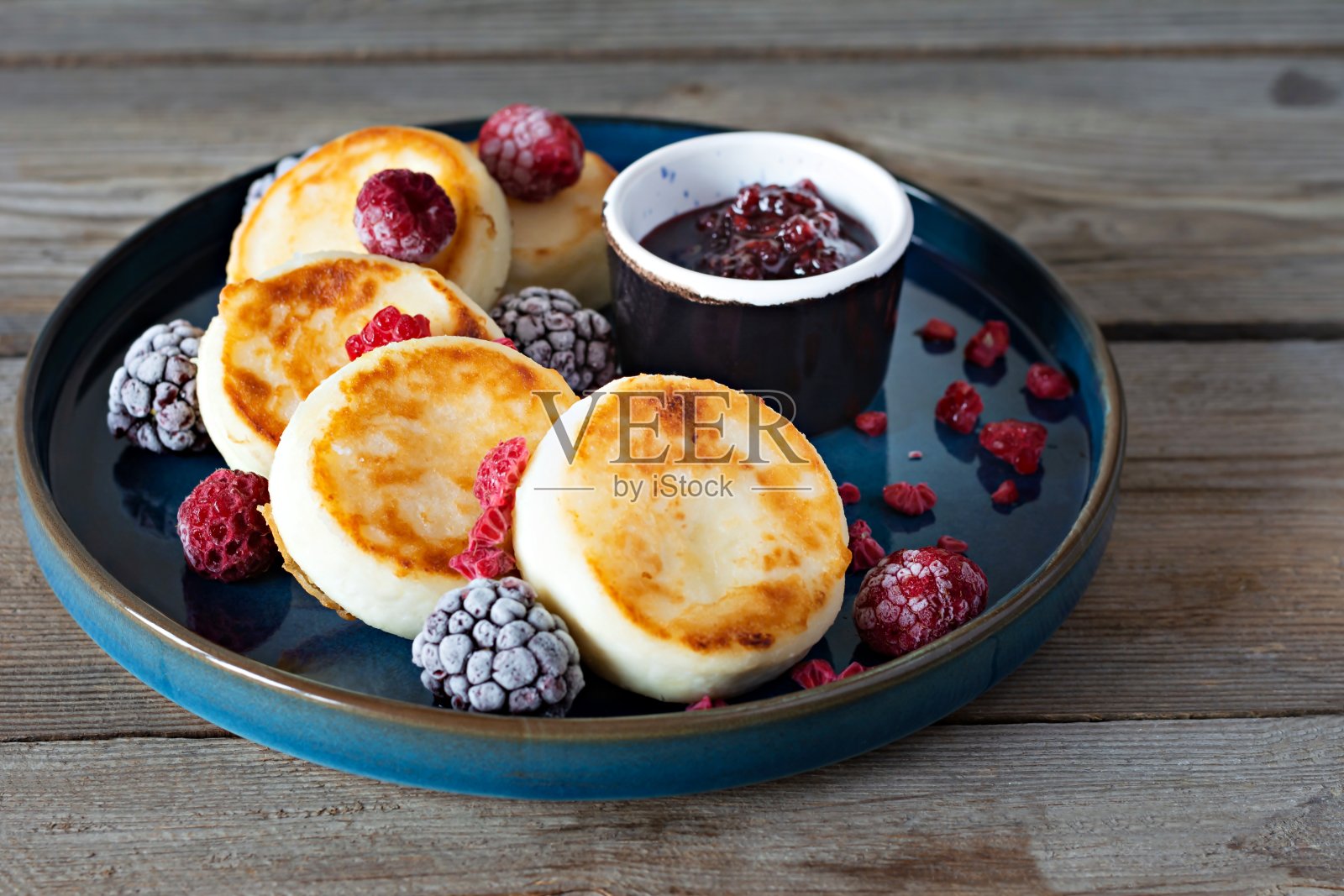 蓝色盘子里放着新鲜的白软干酪或乳清干酪煎饼，配上新鲜的浆果和果酱。照片摄影图片