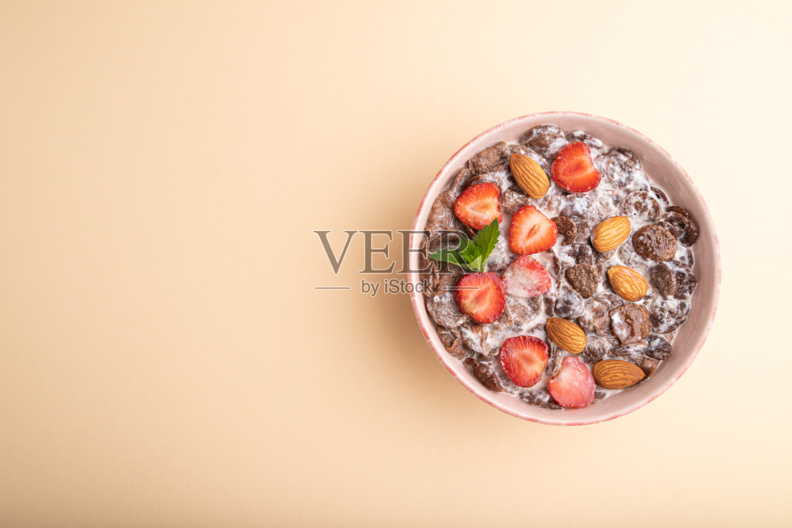 巧克力玉米片与牛奶，草莓和杏仁在陶瓷碗，淡橙色背景。俯视图，复制空间。照片摄影图片