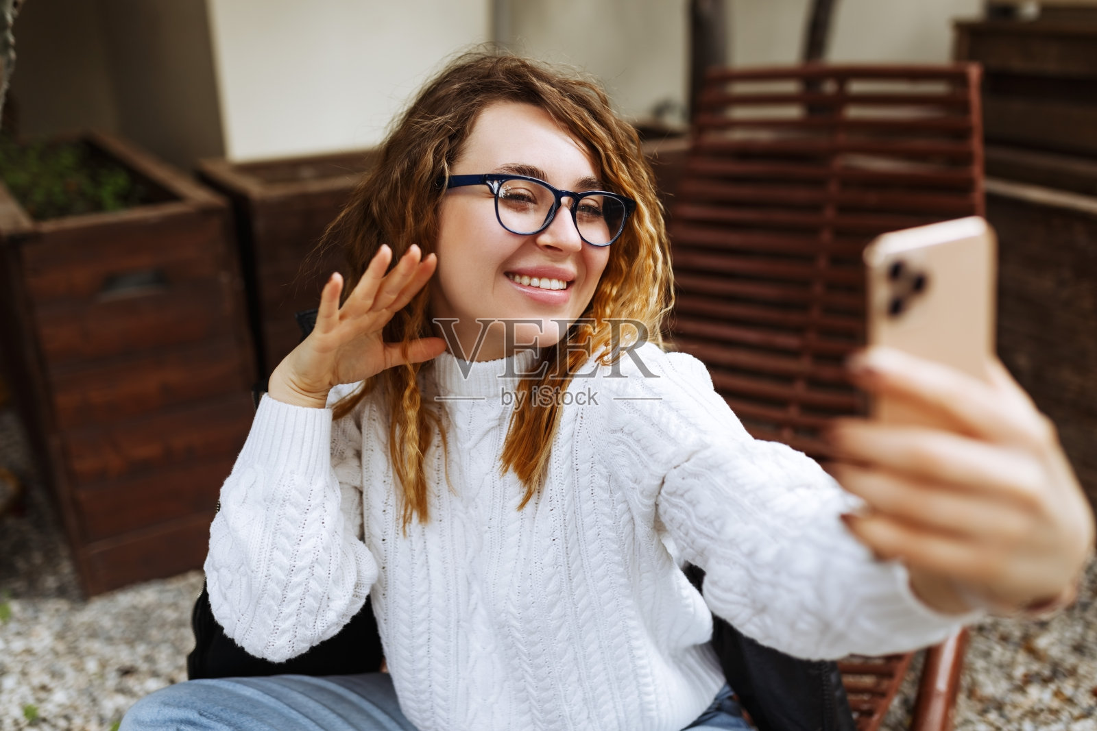 年轻快乐的白种人、千禧一代或z一代女性，深色长发，手里拿着智能手机，在现代的户外咖啡馆里拍摄社交媒体博客。使用社交网络的潮人网红照片摄影图片