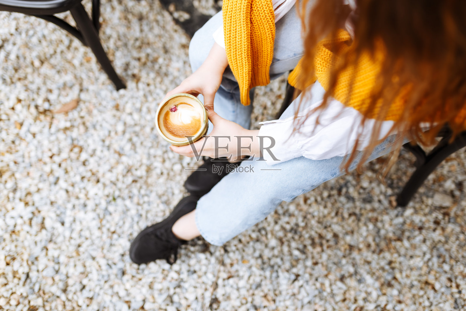 女人穿着休闲的衣服，拿着一杯卡布奇诺咖啡，个人的观点。俯视图照片摄影图片