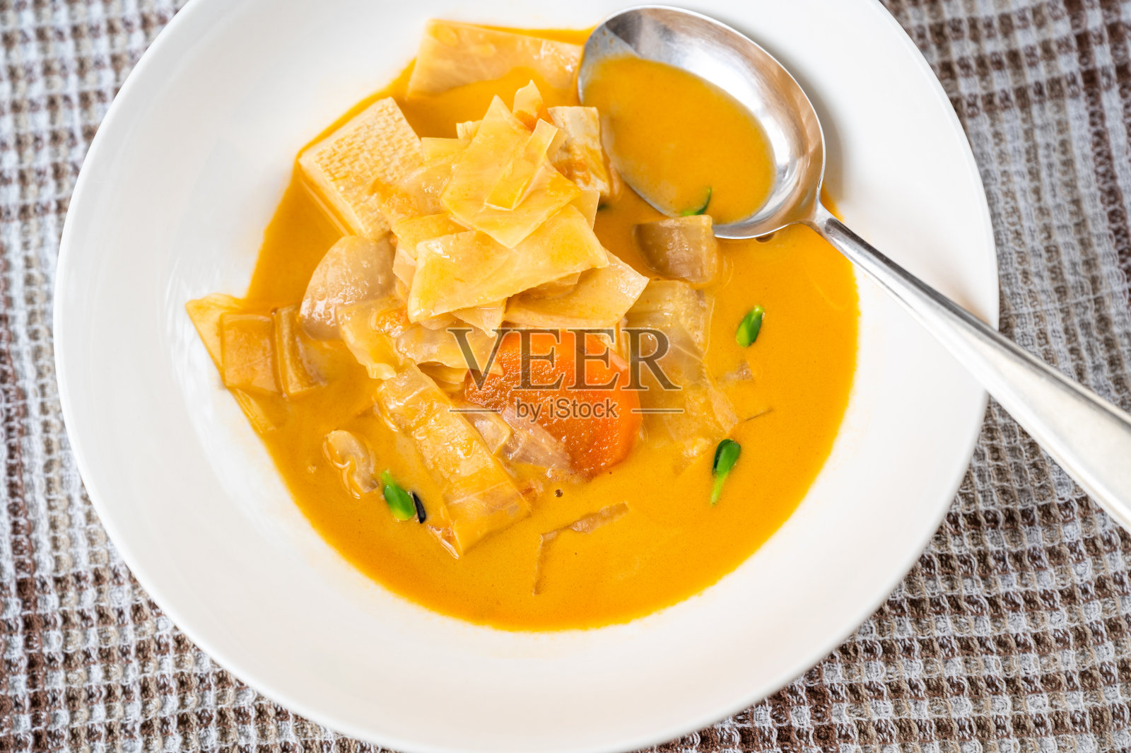 椰子汁汤加竹笋，豆腐，洋葱和胡萝卜在盘子里，勺子。照片摄影图片