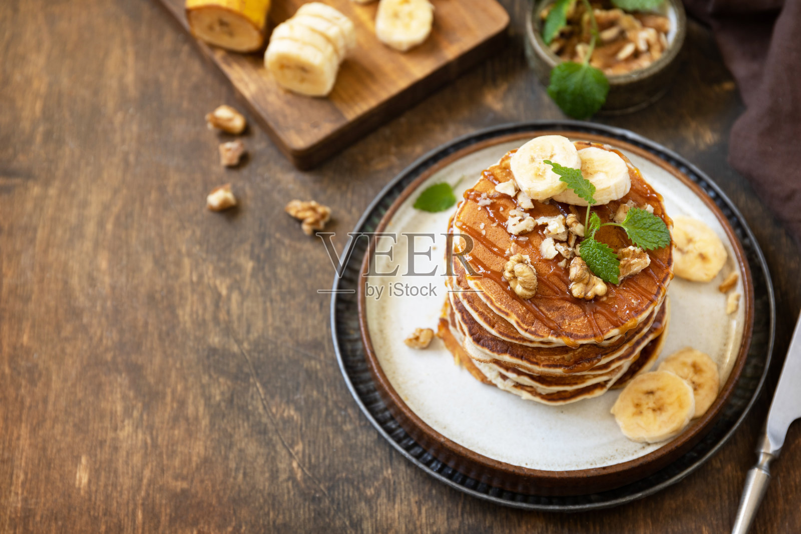 庆祝煎饼节，美式早餐。在质朴的木桌上，美味的自制香蕉煎饼配坚果和焦糖。副本的空间。照片摄影图片