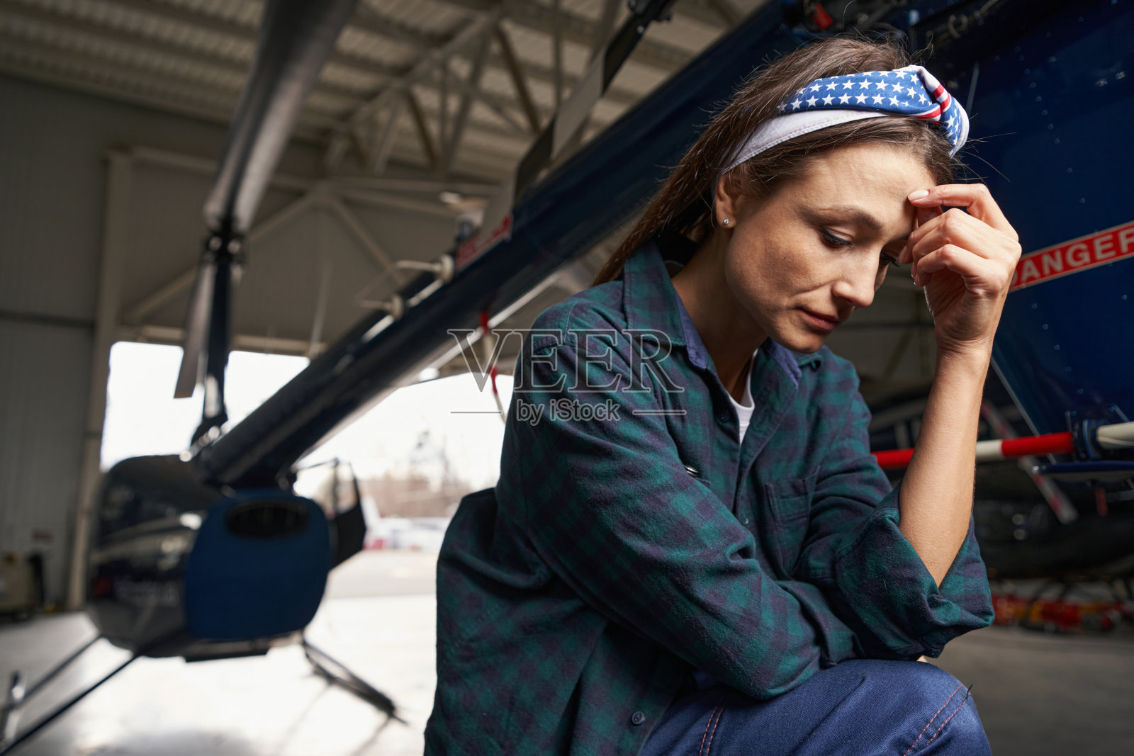 美丽体贴的女人救济工程师坐在飞机前的机库照片摄影图片