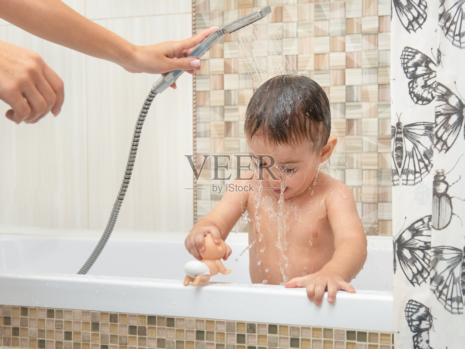 小男孩站在淋浴的水流下。儿童居家卫生保健的概念。在浴室里洗澡的孩子的肖像。棕色的眼睛睁得大大的。照片摄影图片