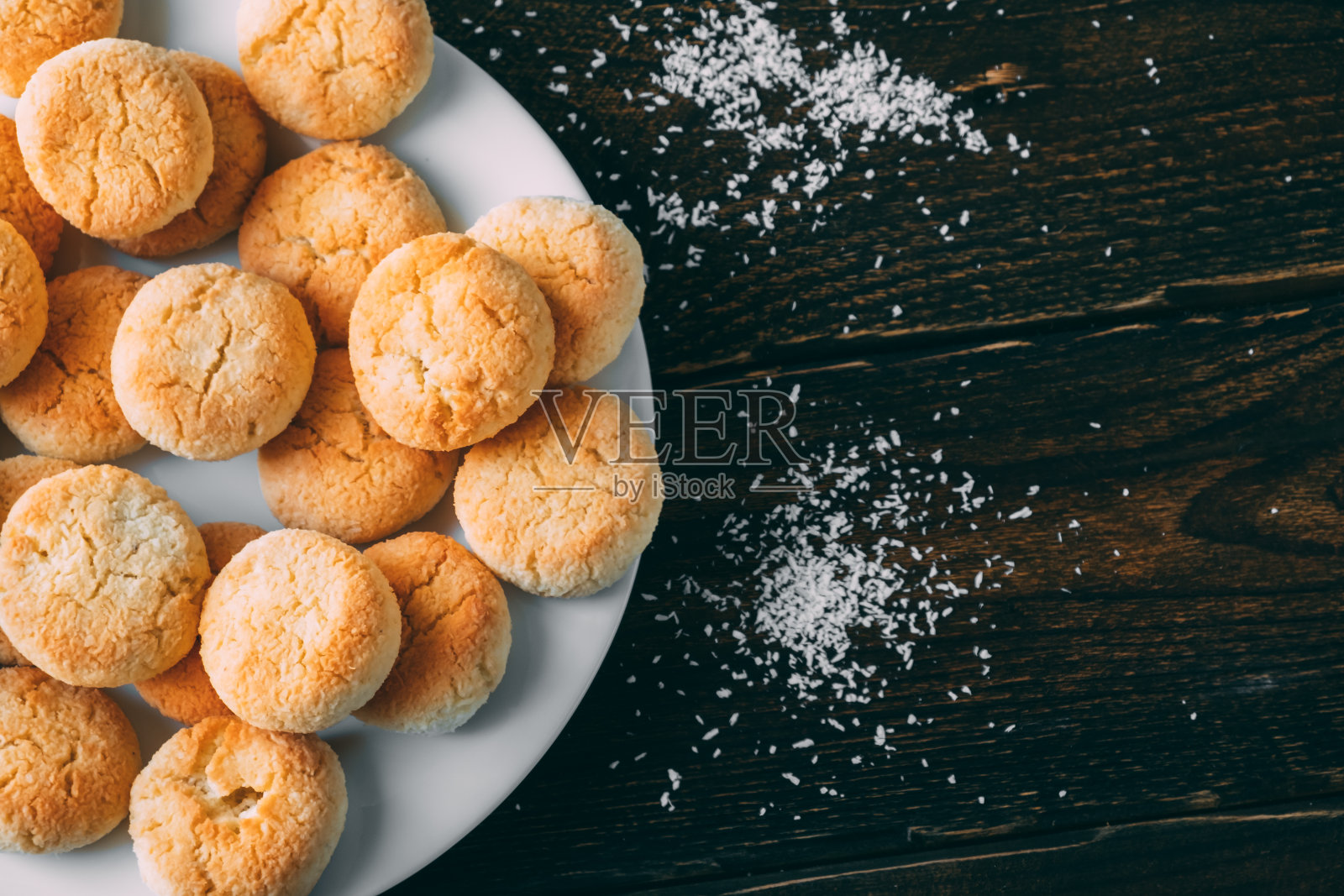 木桌上白色盘子里的自制椰子饼干。照片摄影图片