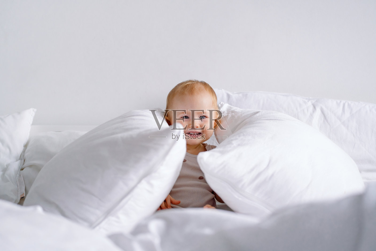 微笑的孩子在床上有很多枕头玩得很开心。玩捉迷藏或偷看嘘嘘的婴儿。照片摄影图片