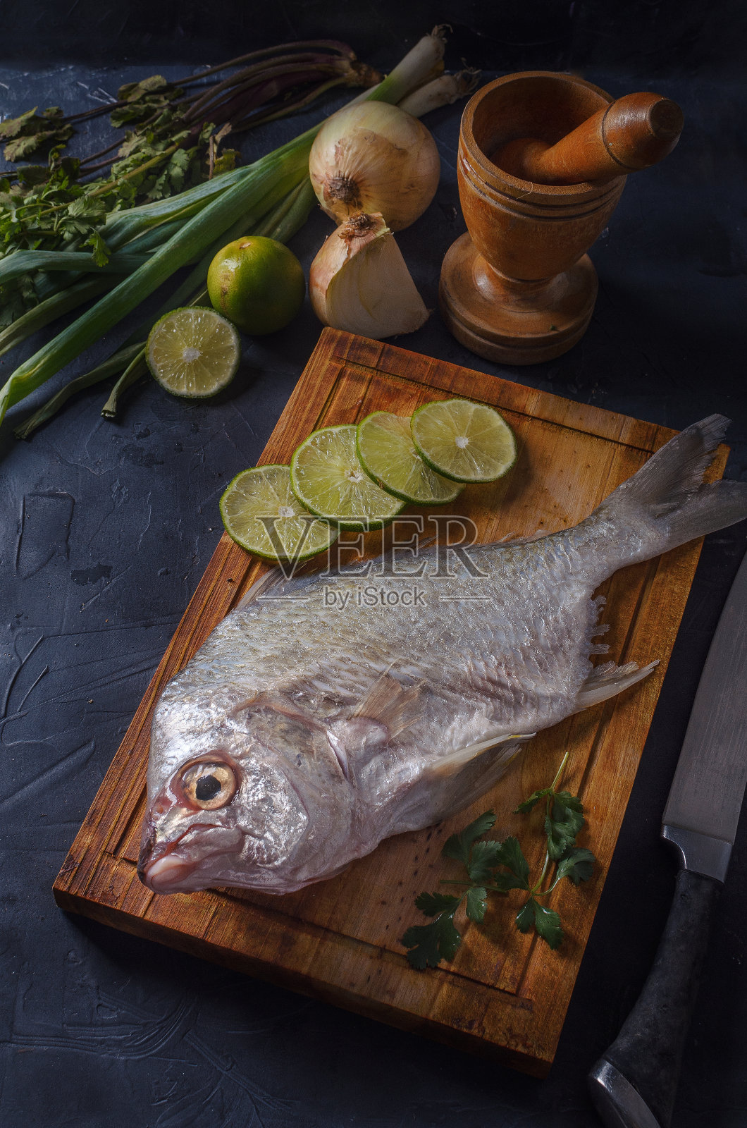 新鲜的鱼在黑色的木板背景与洋葱和柠檬照片摄影图片