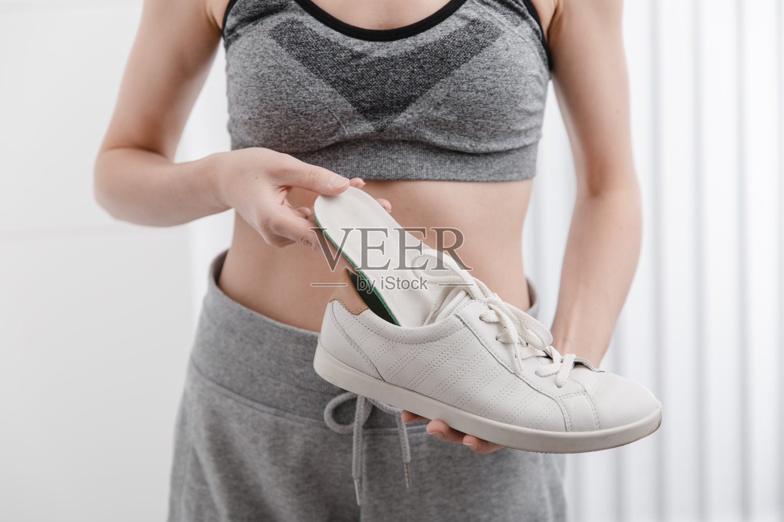 妇女在家里把矫形鞋垫放进鞋里。运动女孩适合矫形鞋垫在室内，关闭。足部护理横幅。扁平足的修正。足部疾病的治疗和预防照片摄影图片