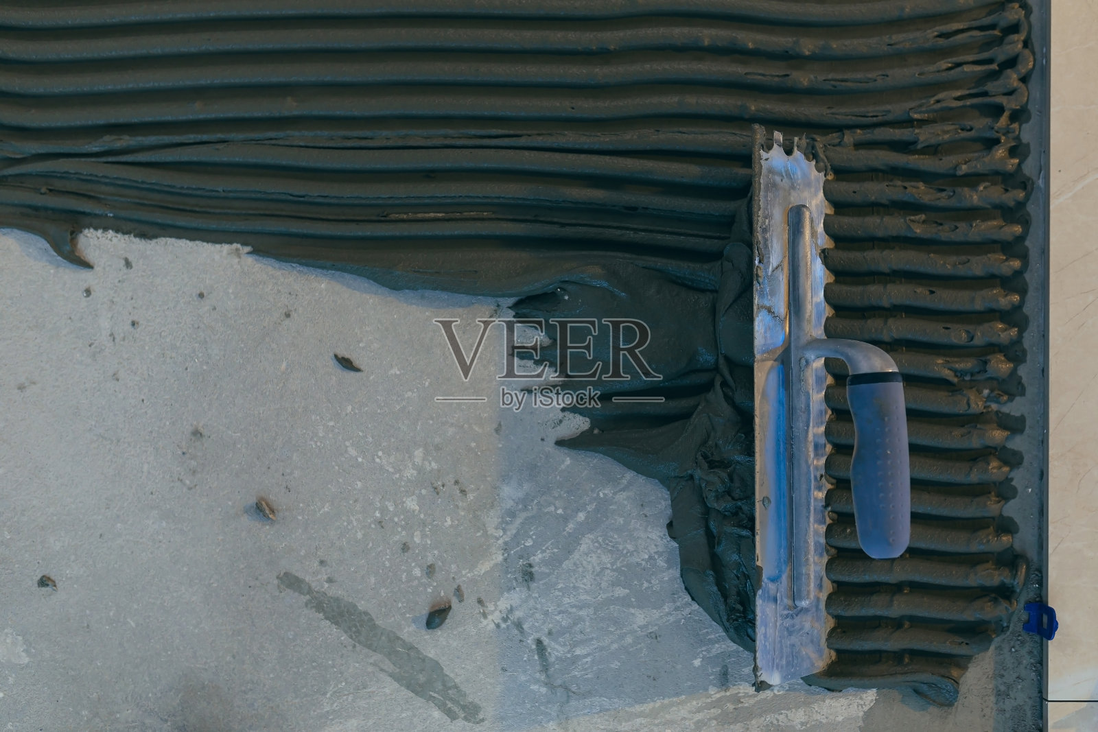 近距离拍摄一位建筑大师的手，用带槽的泥铲，将瓷砖粘合剂混合，进行瓷砖的安装照片摄影图片