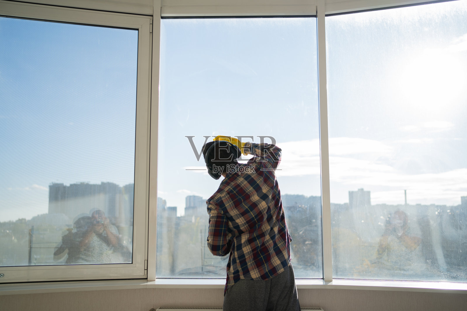 男人戴着耳机在家洗窗户，便装衬衫，黄色橡胶手套，家居清洁概念。照片摄影图片