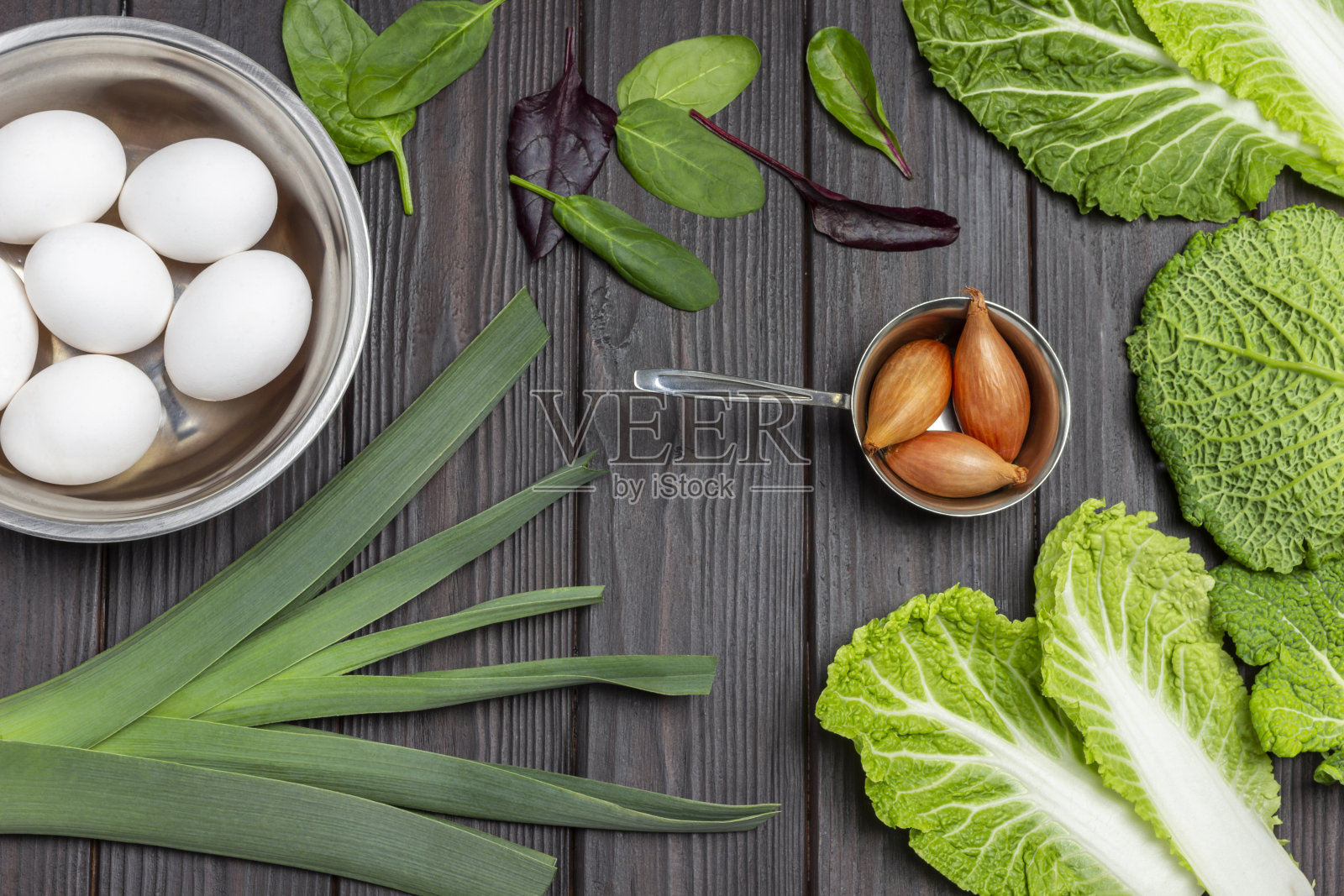 金属碗里的鸡蛋，韭菜和青葱，菠菜叶和卷心菜。照片摄影图片