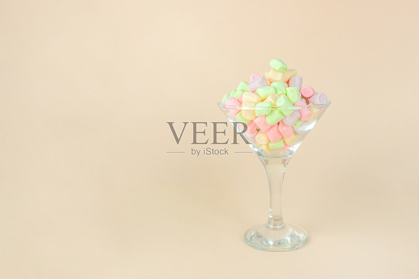 明亮的棉花糖为甜打破在柔和的米色背景上的葡萄酒杯。照片摄影图片